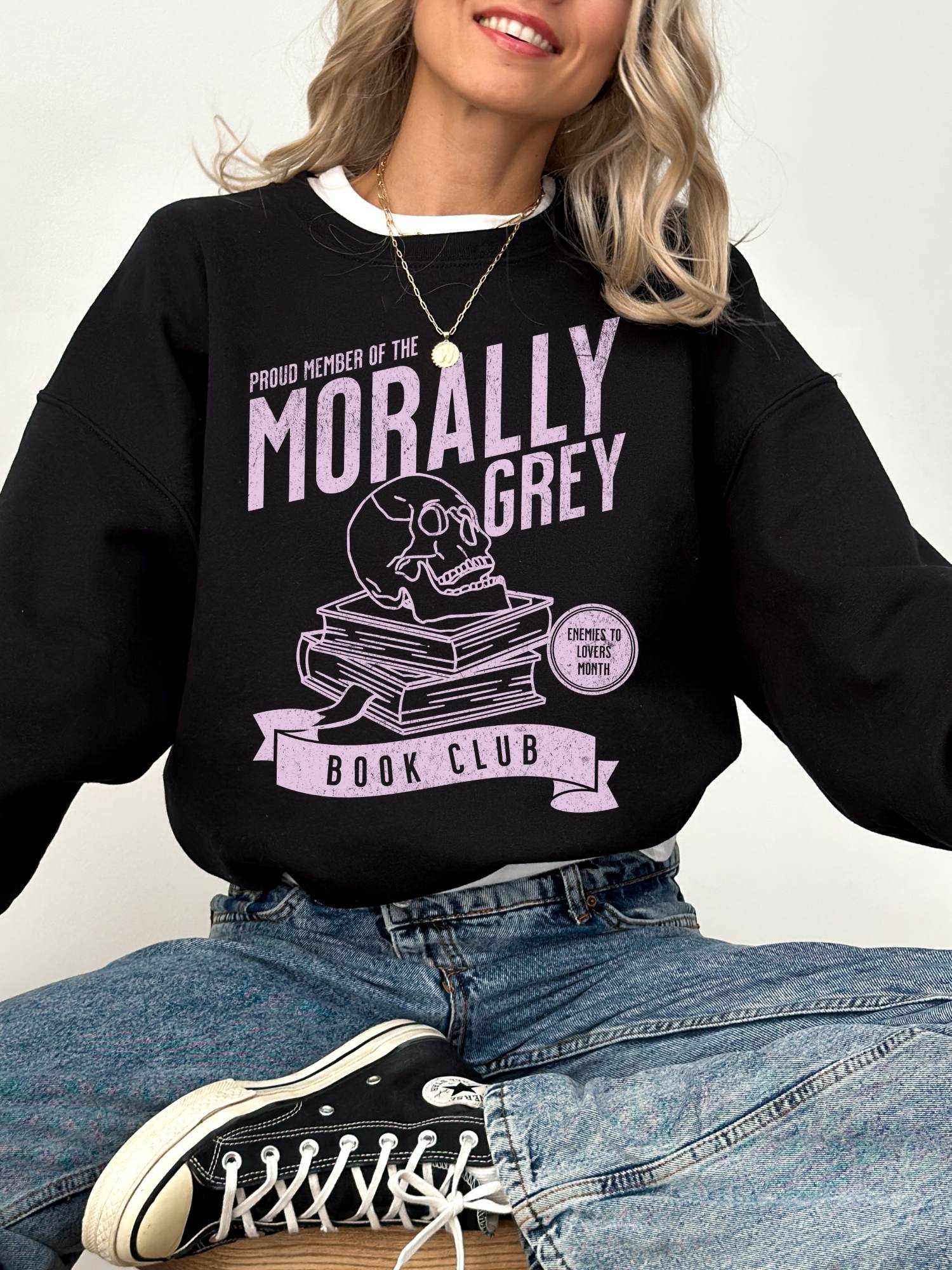 woman sitting in black sweatshirt with purple morally grey book club print featuring skull and books