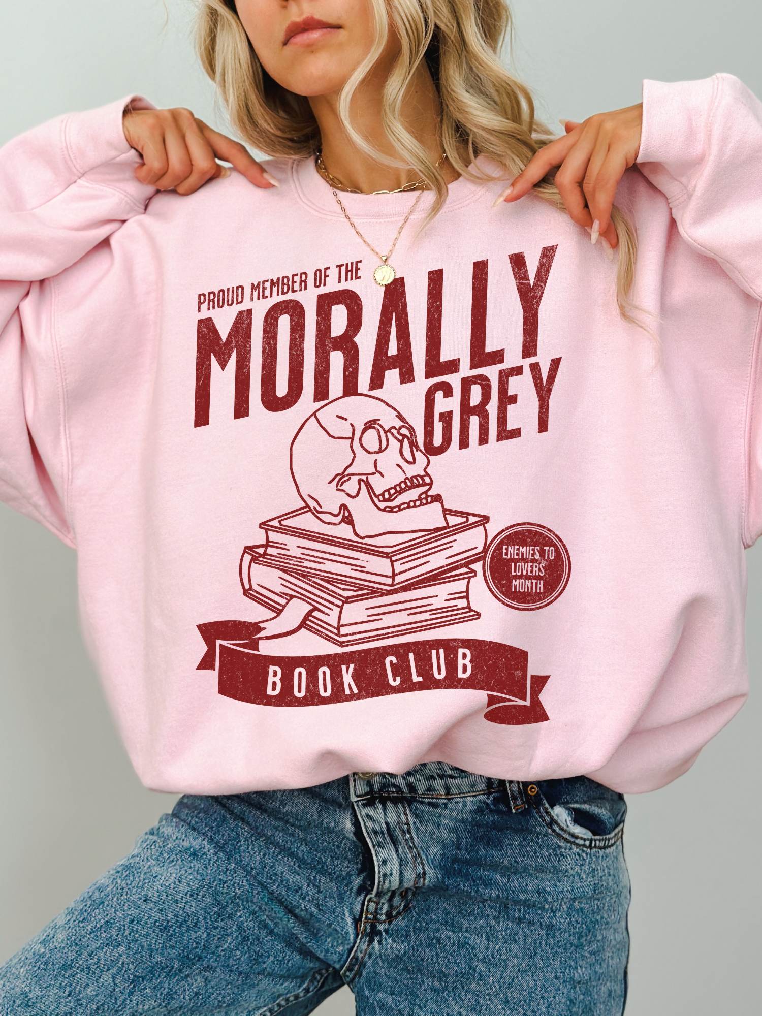 woman wearing pink sweatshirt with distressed red morally grey book club graphic and enemies to lovers badge