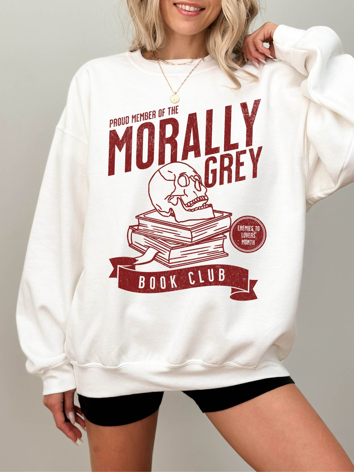 woman wearing white sweatshirt with red skull and books design reading morally grey book club