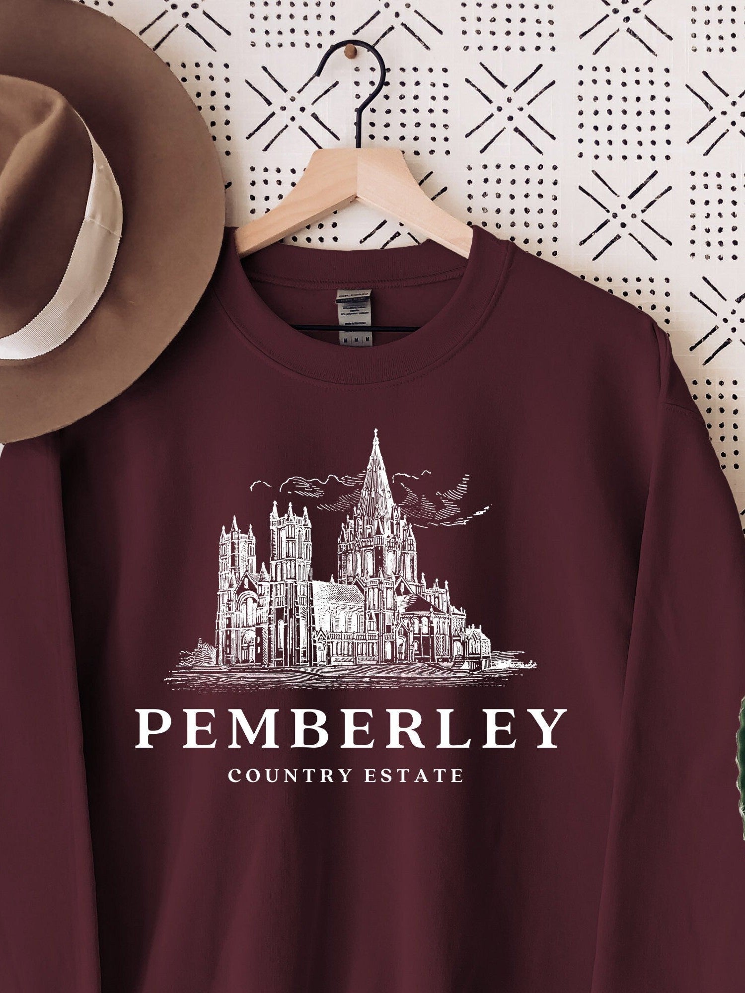 maroon sweatshirt on hanger with white Pemberley country estate design and fedora hat