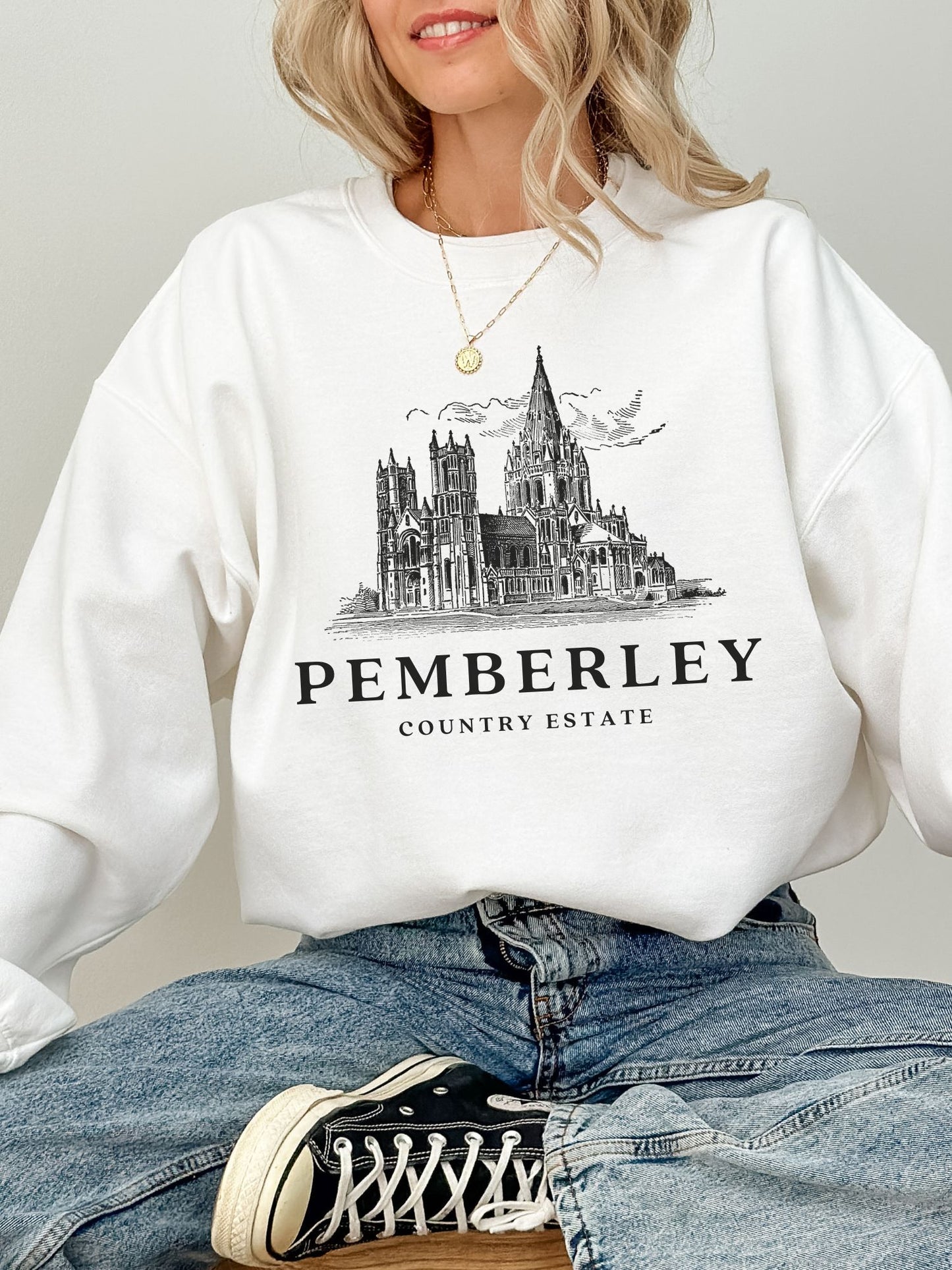 woman sitting in white sweatshirt with vintage line art of Pemberley estate and sneakers