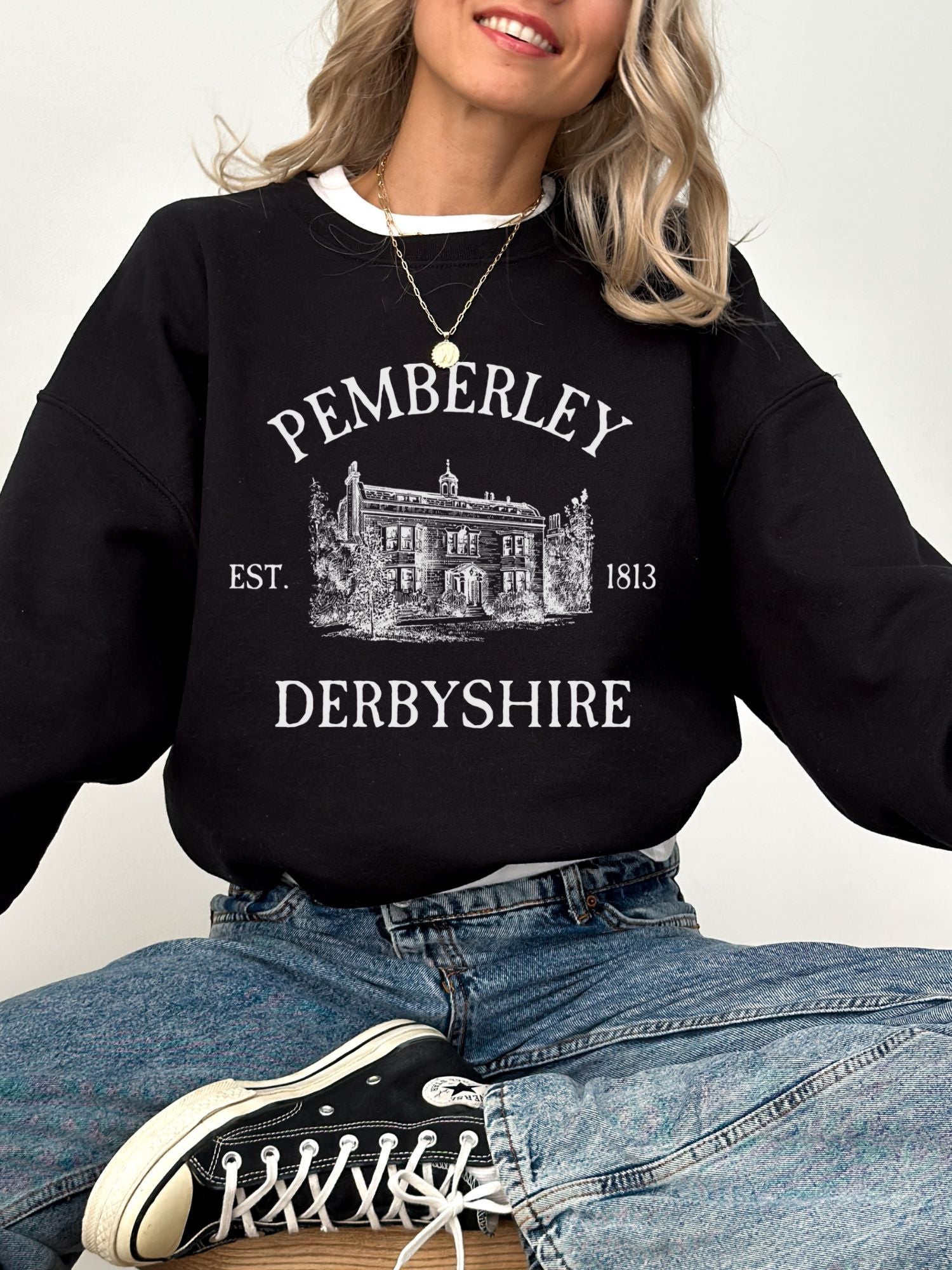 woman wearing black crewneck sweatshirt with white print of Pemberley estate and Derbyshire text