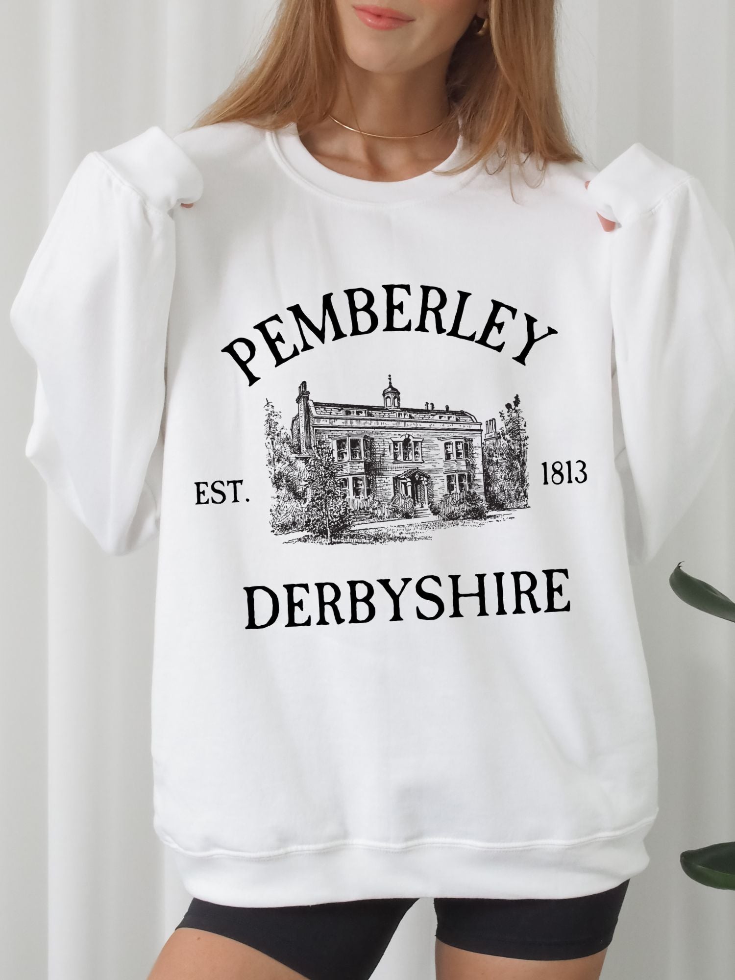 woman wearing white sweatshirt with black Pemberley Derbyshire print and sketch of estate