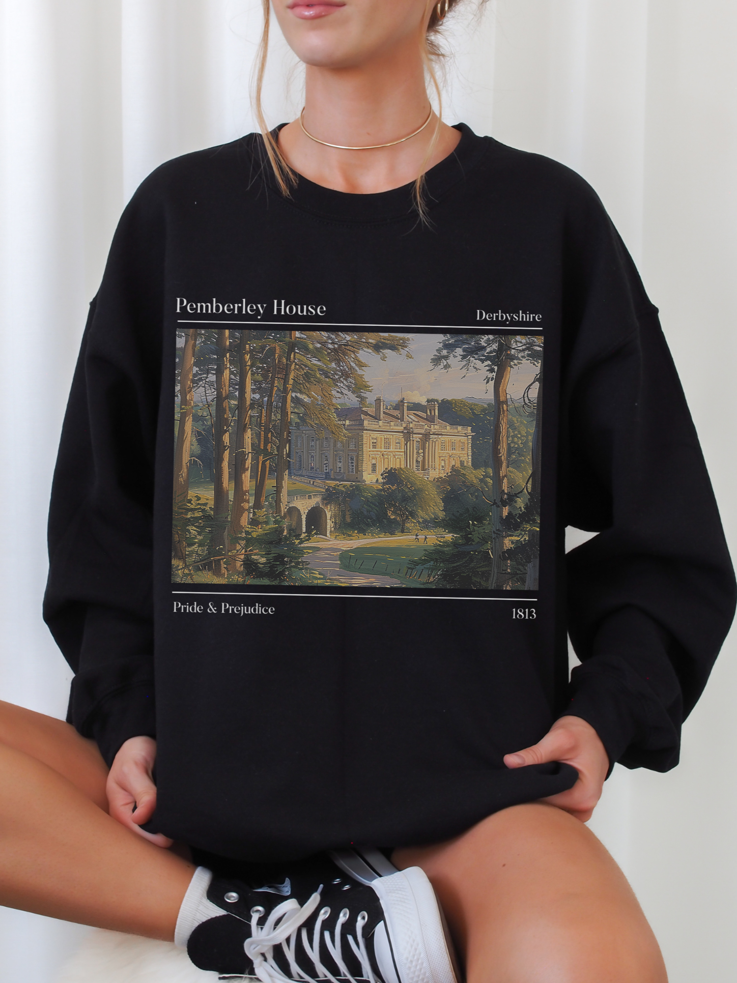 seated woman in black Pemberley House sweatshirt featuring illustration from Pride & Prejudice