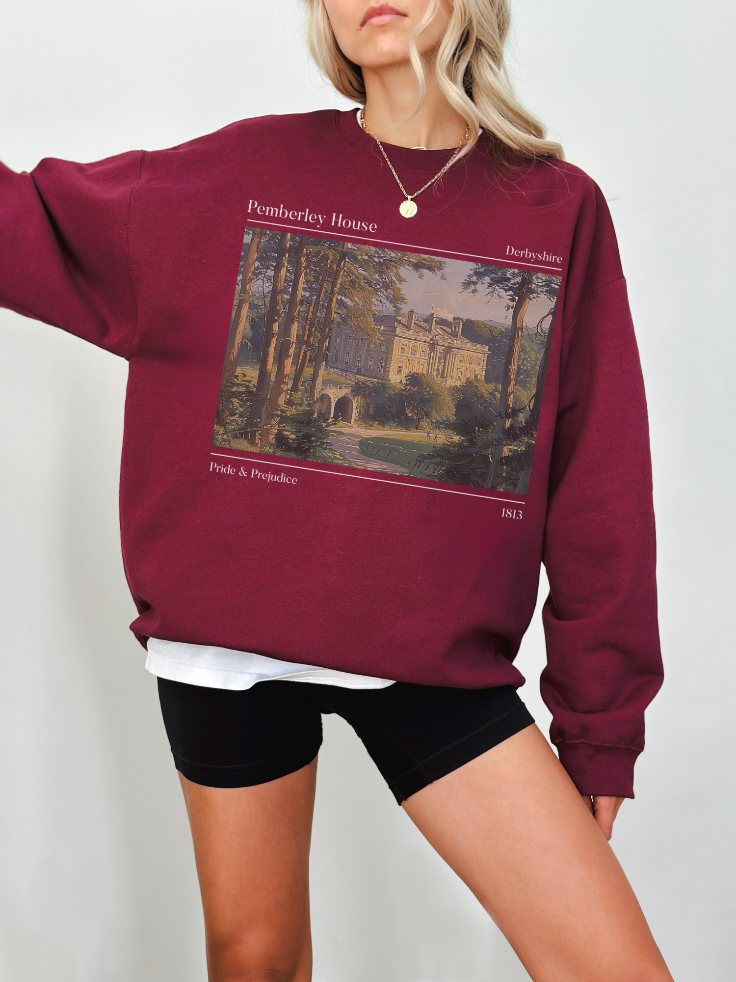woman wearing maroon sweatshirt with vintage painting of Pemberley House from Pride & Prejudice
