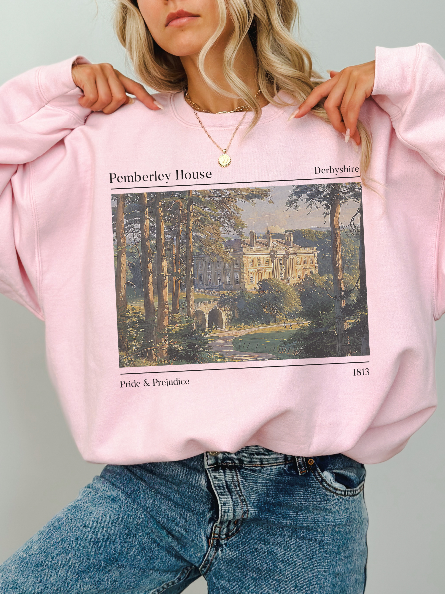 woman wearing light pink Pride & Prejudice sweatshirt with vintage-style illustration of Pemberley House