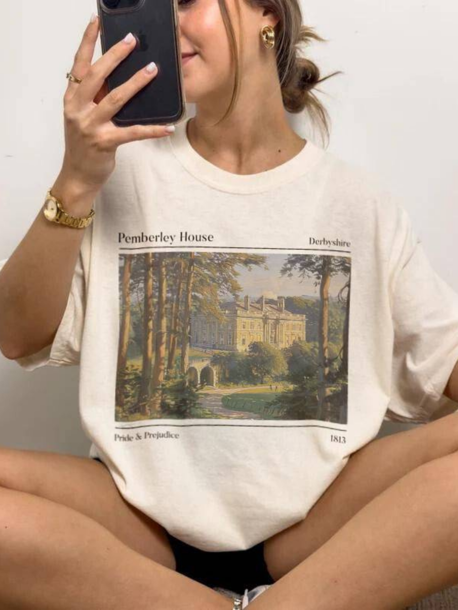 woman sitting in natural color t-shirt with classic painting of Pemberley and 1813 Pride & Prejudice text