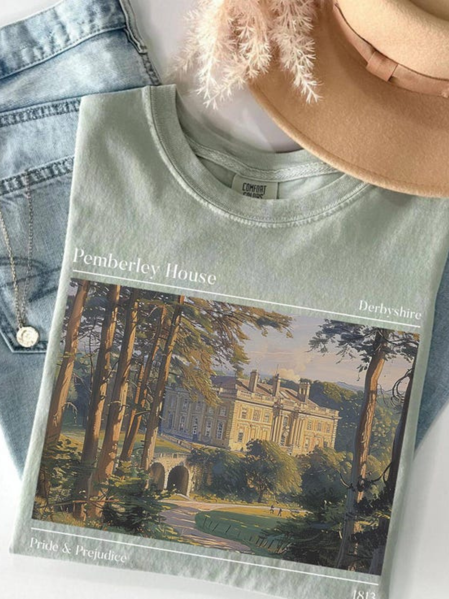 flat lay of sage green Pemberley House t-shirt with vintage Pride & Prejudice artwork styled with denim