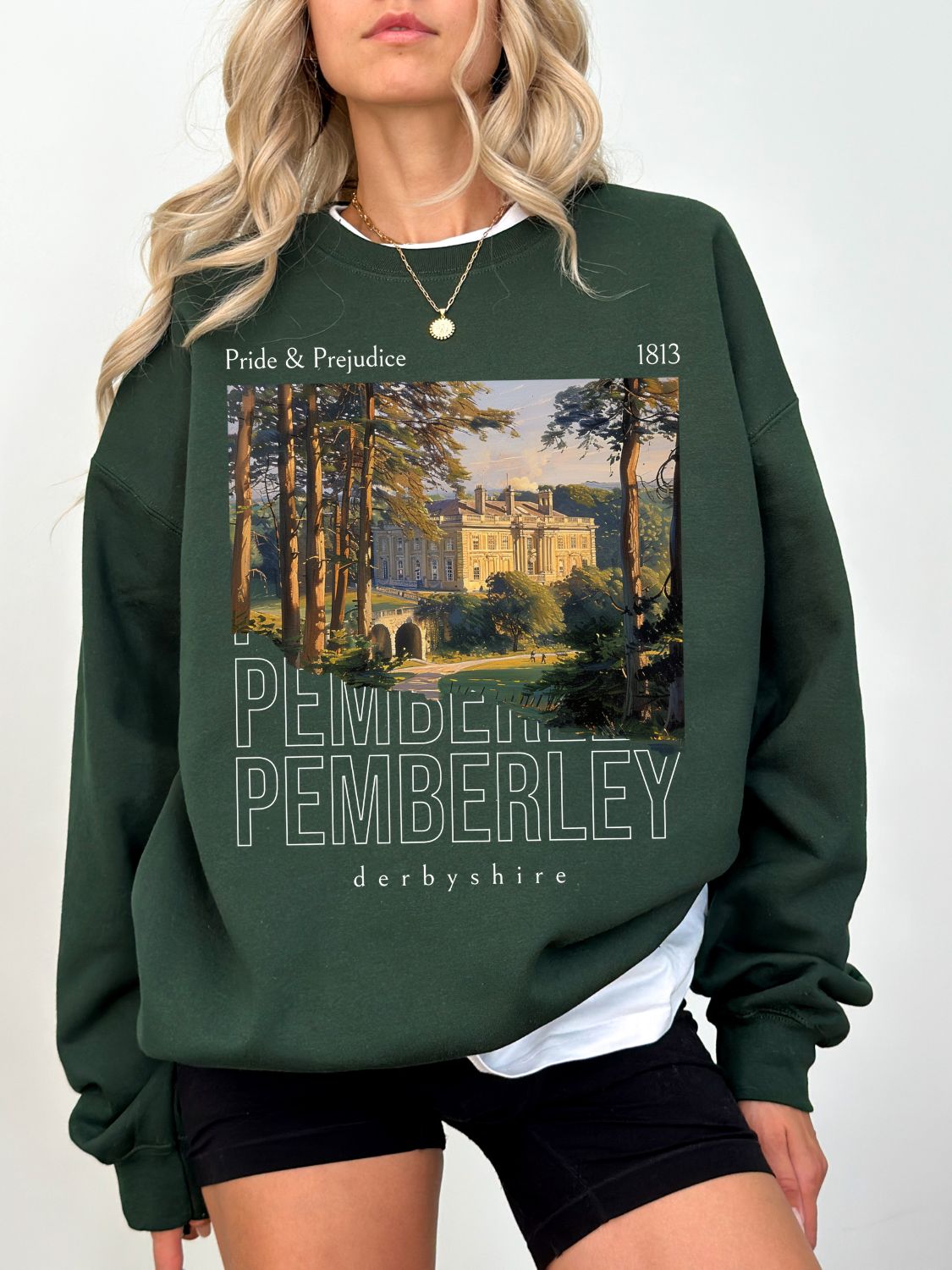 woman wearing forest green sweatshirt with Pride and Prejudice design featuring Pemberley estate painting