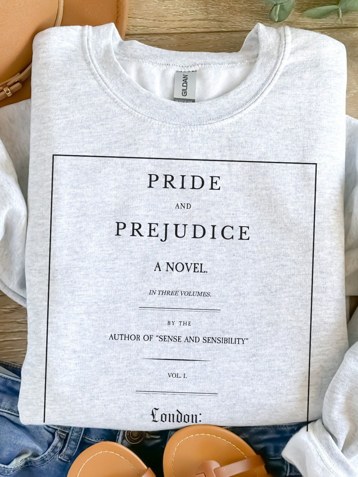 folded ash grey sweatshirt with black Pride and Prejudice title page design styled with jeans and sandals