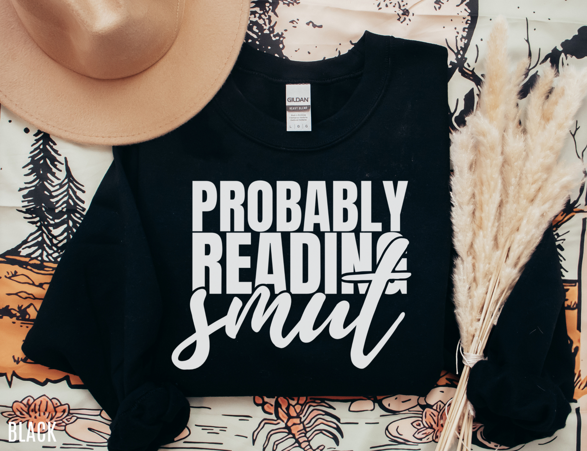flat lay of black Probably Reading Smut sweatshirt styled with hat and pampas grass