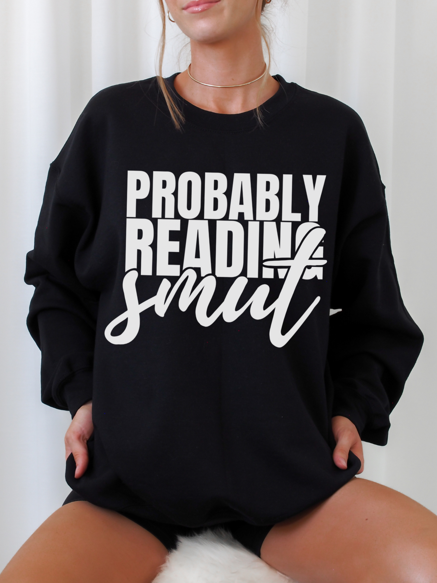 woman sitting in oversized black Probably Reading Smut sweatshirt with bold white text