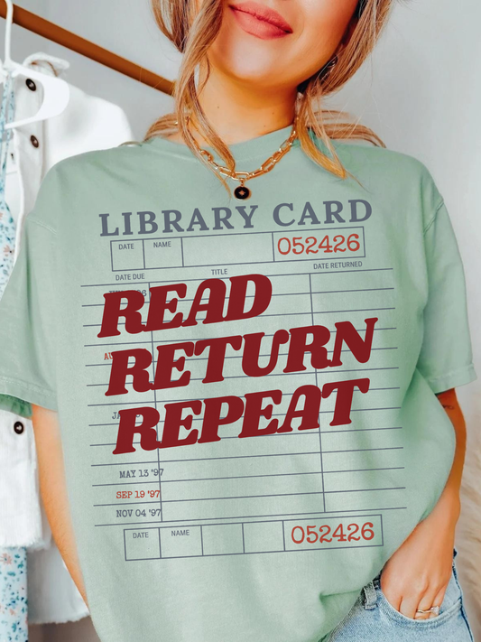 woman wearing a bay Comfort Colors shirt featuring a vintage library card graphic with the phrase read return repeat in bold red lettering, styled with a gold necklace and casual denim for a cozy book lover aesthetic
