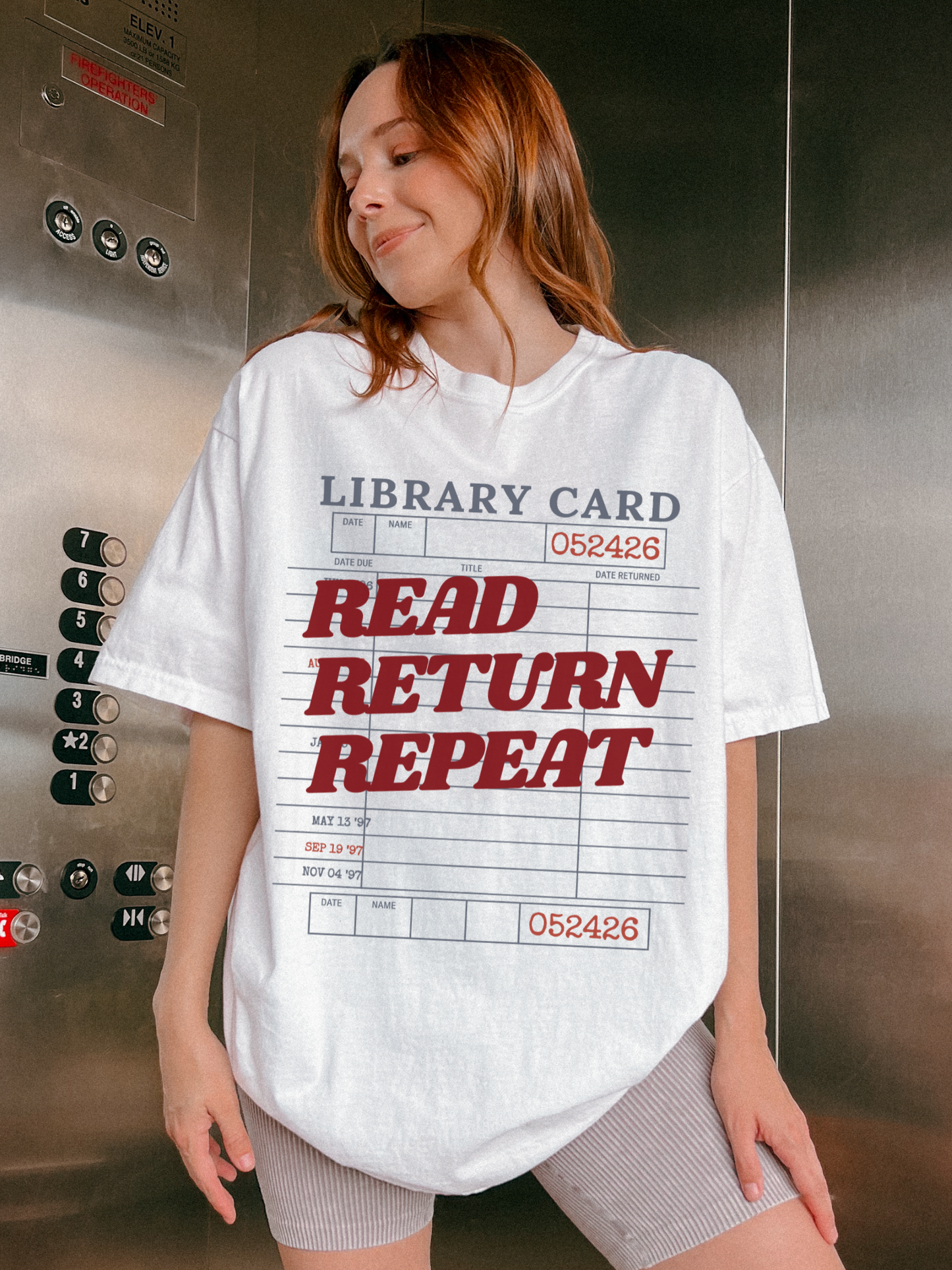 woman wearing a white Comfort Colors shirt featuring a vintage library card read return repeat design in an elevator setting, oversized reader graphic tee perfect for librarians bookworms and reading enthusiasts