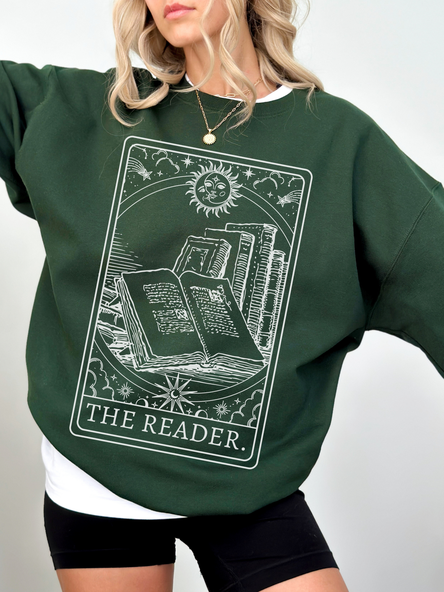 woman wearing a forest green sweatshirt featuring tarot card artwork of books with sun and stars