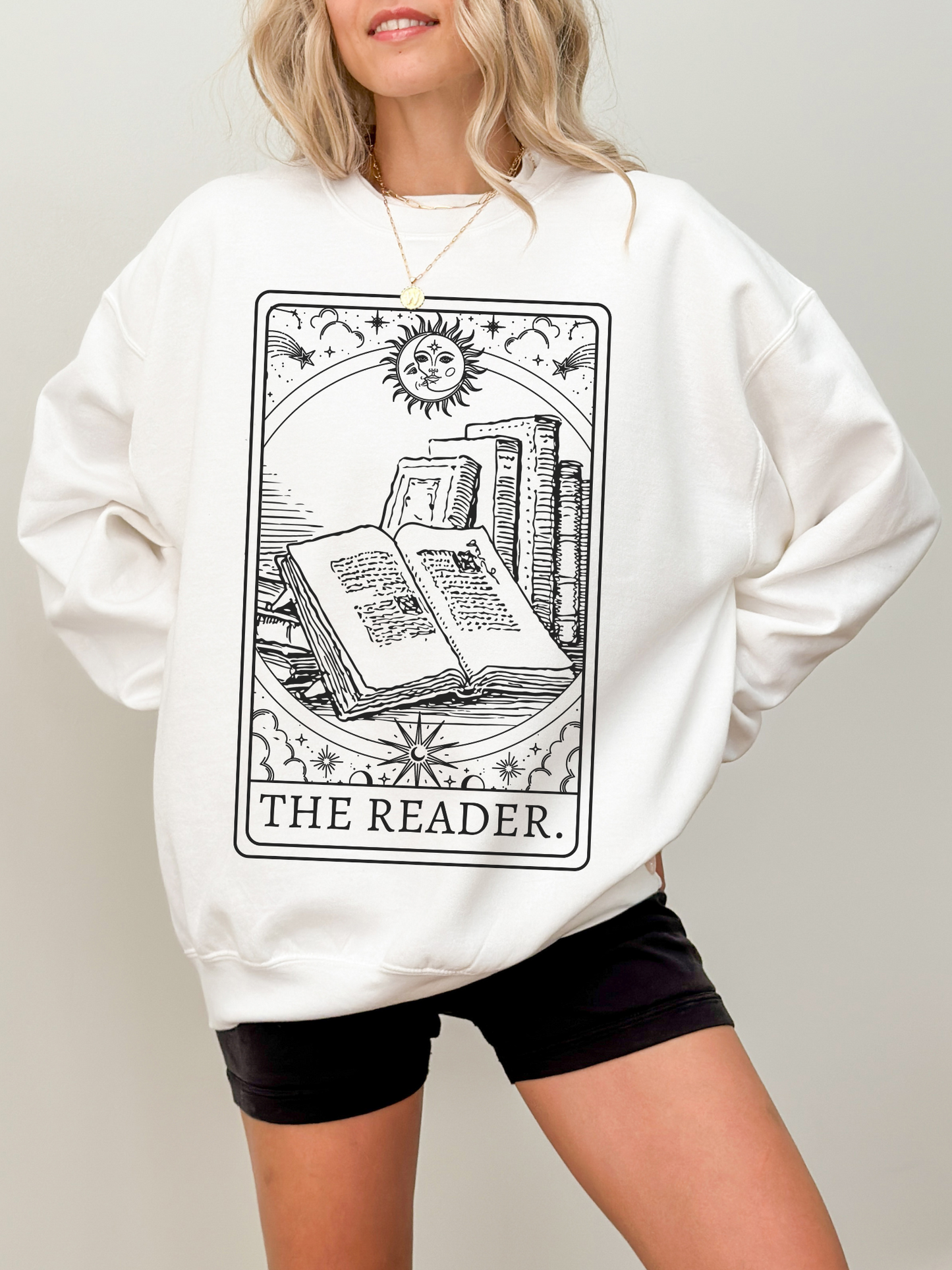 woman in white sweatshirt showing open book tarot print with celestial sun and vintage books