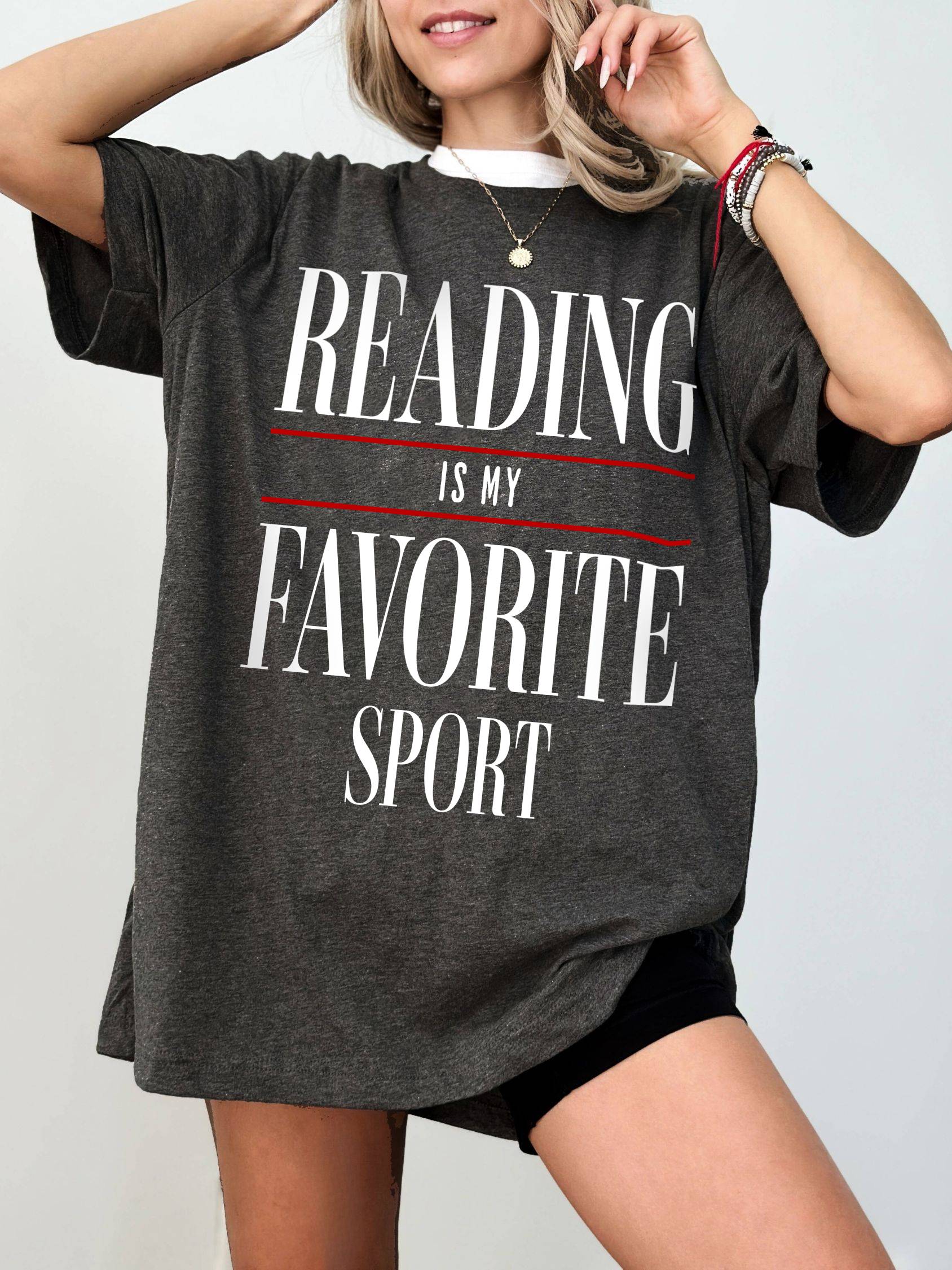 Woman wearing oversized "Reading Is My Favorite Sport" graphic tee in dark heather grey with vintage bold text, smiling casually.