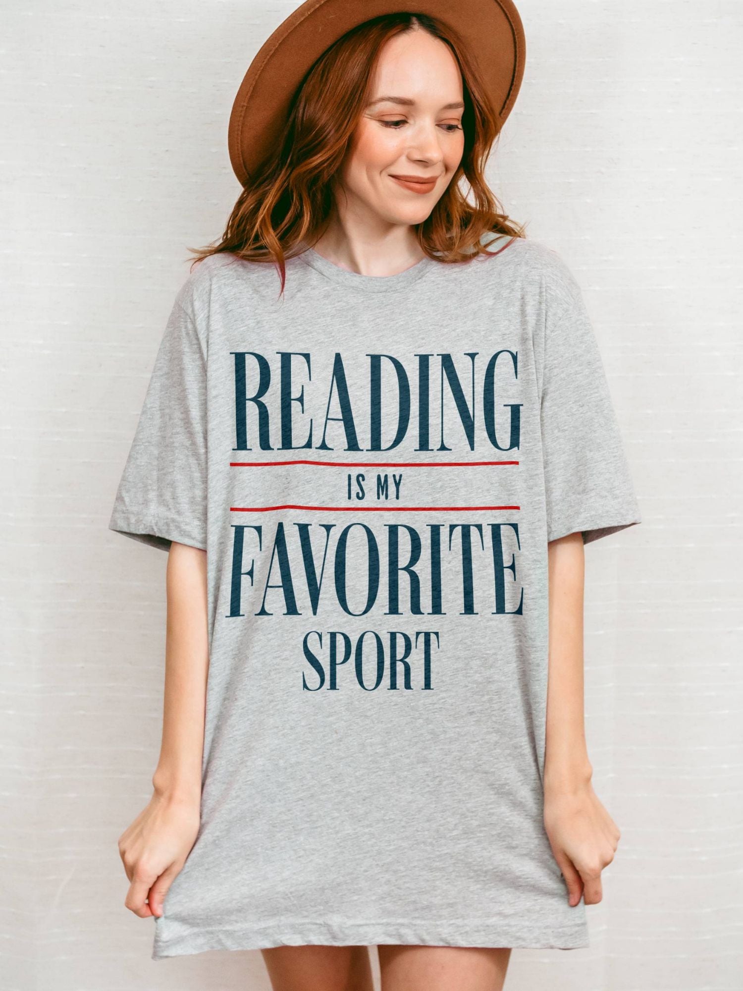 Woman wearing oversized "Reading Is My Favorite Sport" graphic tee in sport grey grey with bold text, smiling casually.