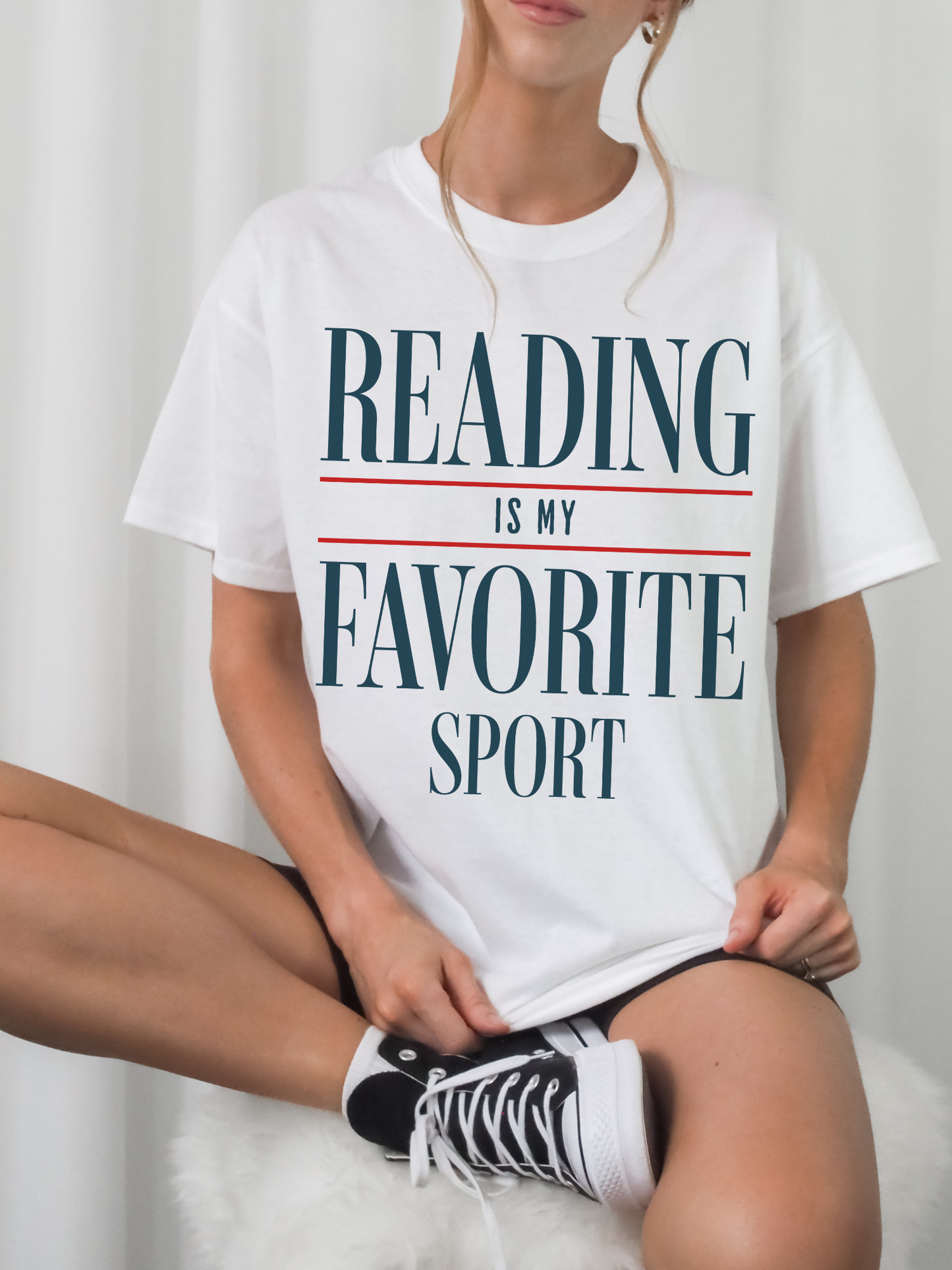woman sitting wearing white reading is my favorite sport t shirt styled with black sneakers and casual cozy book lover outfit