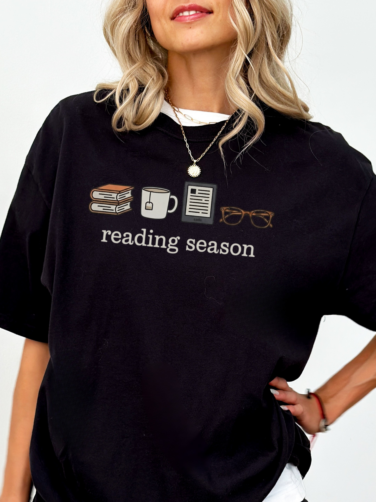 Woman wearing black Reading Season Comfort Colors shirt with cozy bookish icons, layered with white tee underneath