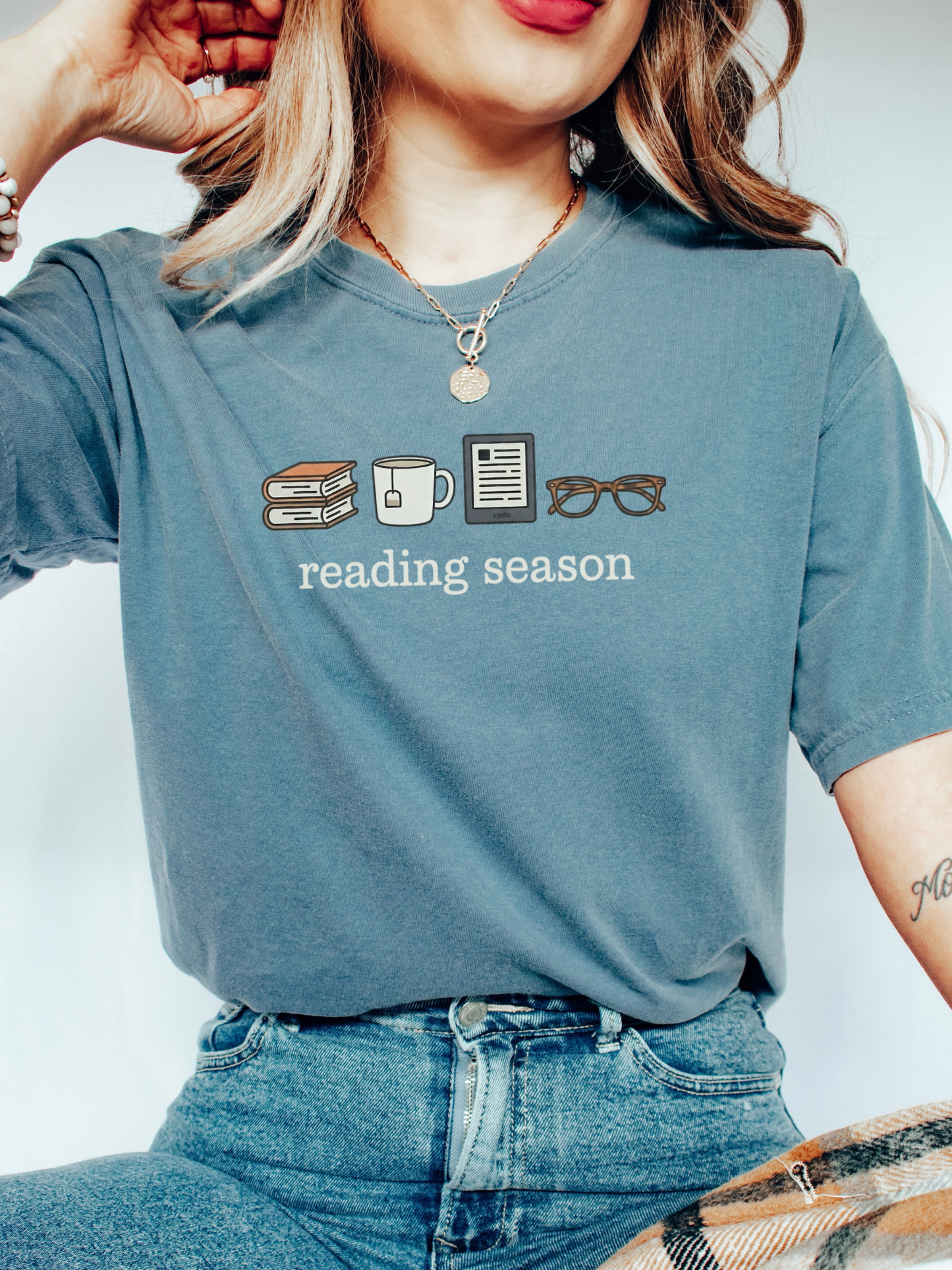 Woman in a blue jean Reading Season shirt with cozy icons for book lovers, sipping tea and reading