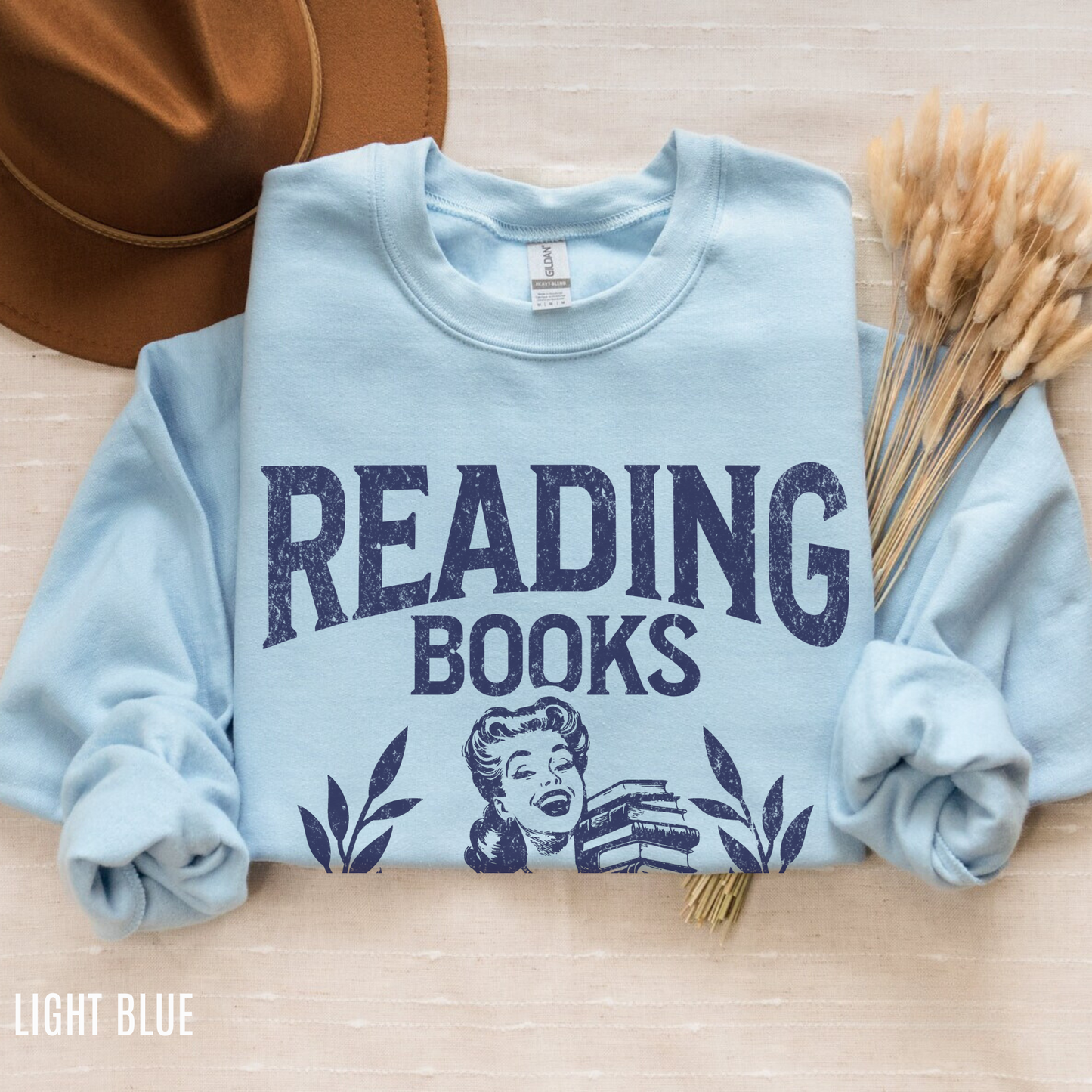 folded light blue sweatshirt with retro design that says reading books is my favorite sport beside hat and wheat bundle