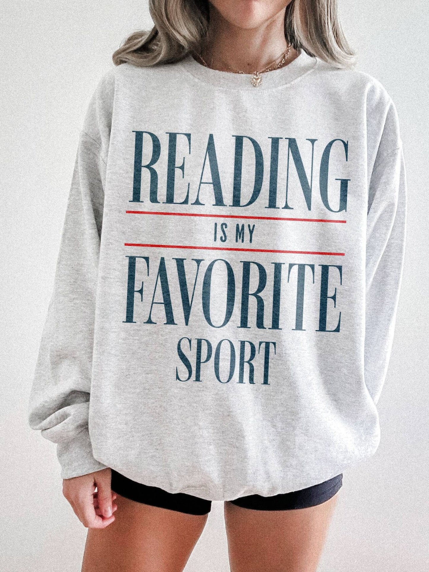 woman standing in ash grey sweatshirt with blue and red reading is my favorite sport lettering