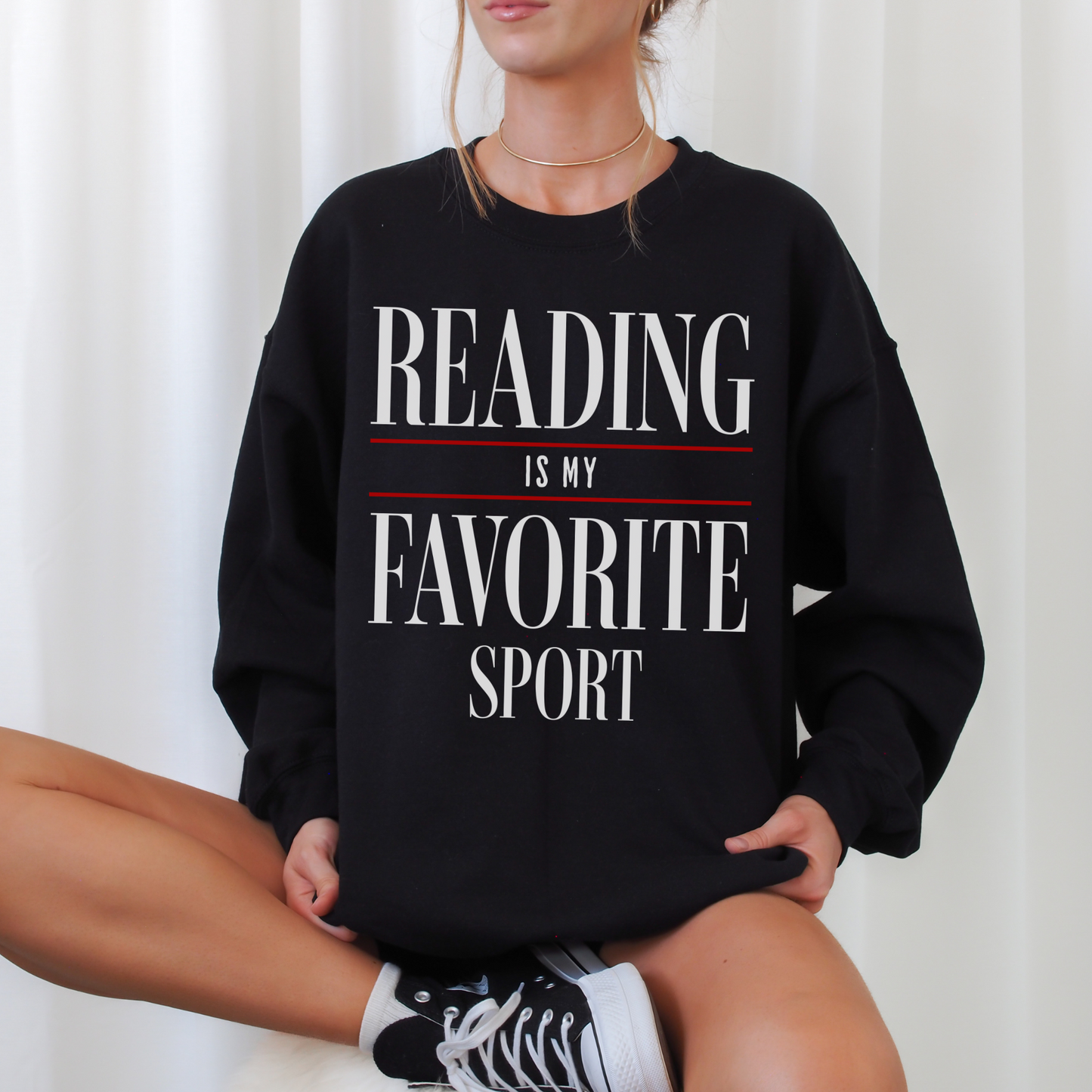 woman sitting cross-legged in black sweatshirt with bold white and red reading is my favorite sport print