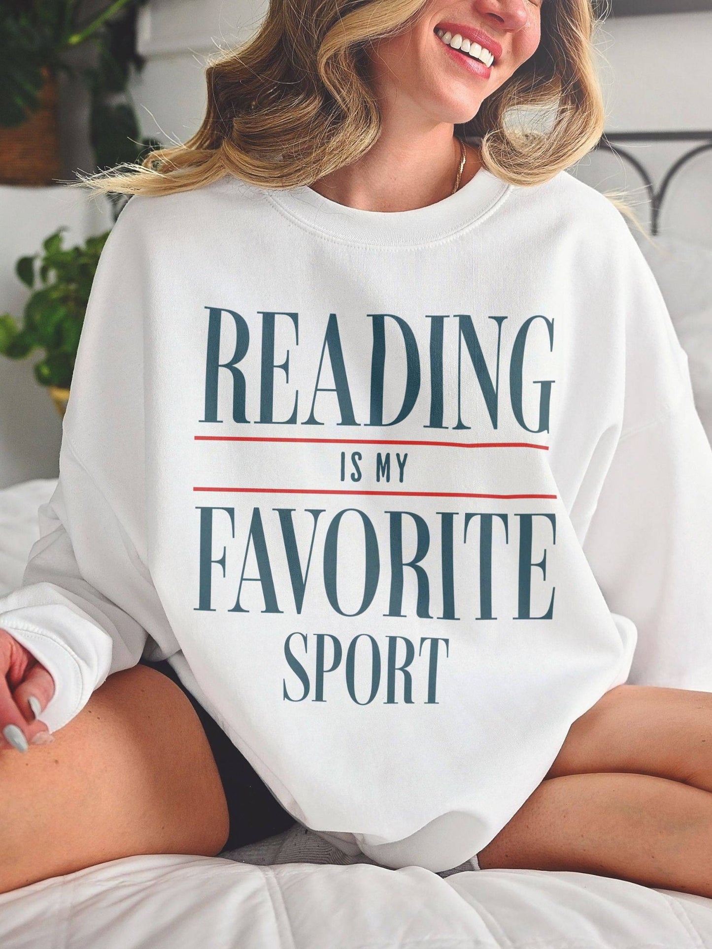 woman smiling on bed wearing a white reading is my favorite sport sweatshirt in bold serif font
