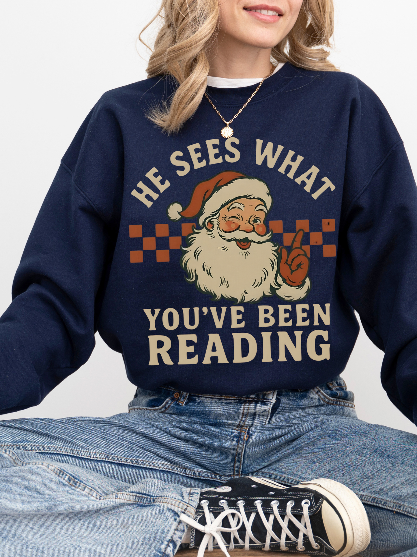 girl sitting cross-legged in navy sweatshirt with vintage santa graphic and bookish quote