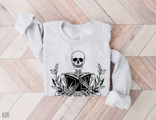 folded ash grey sweatshirt with black line art of skeleton holding an open book