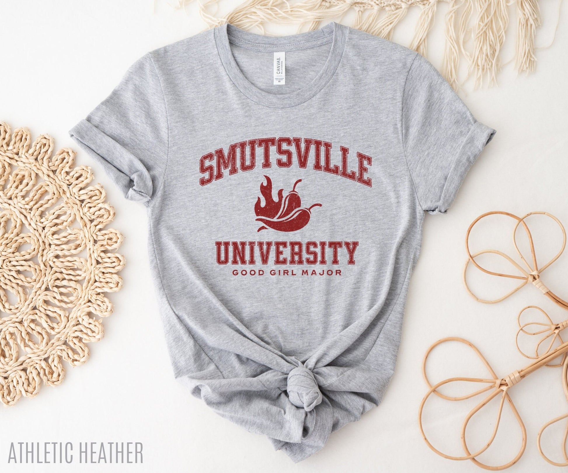 athletic heather t-shirt with red distressed college-style text “Smutsville University,” surrounded by woven and wooden styling props
