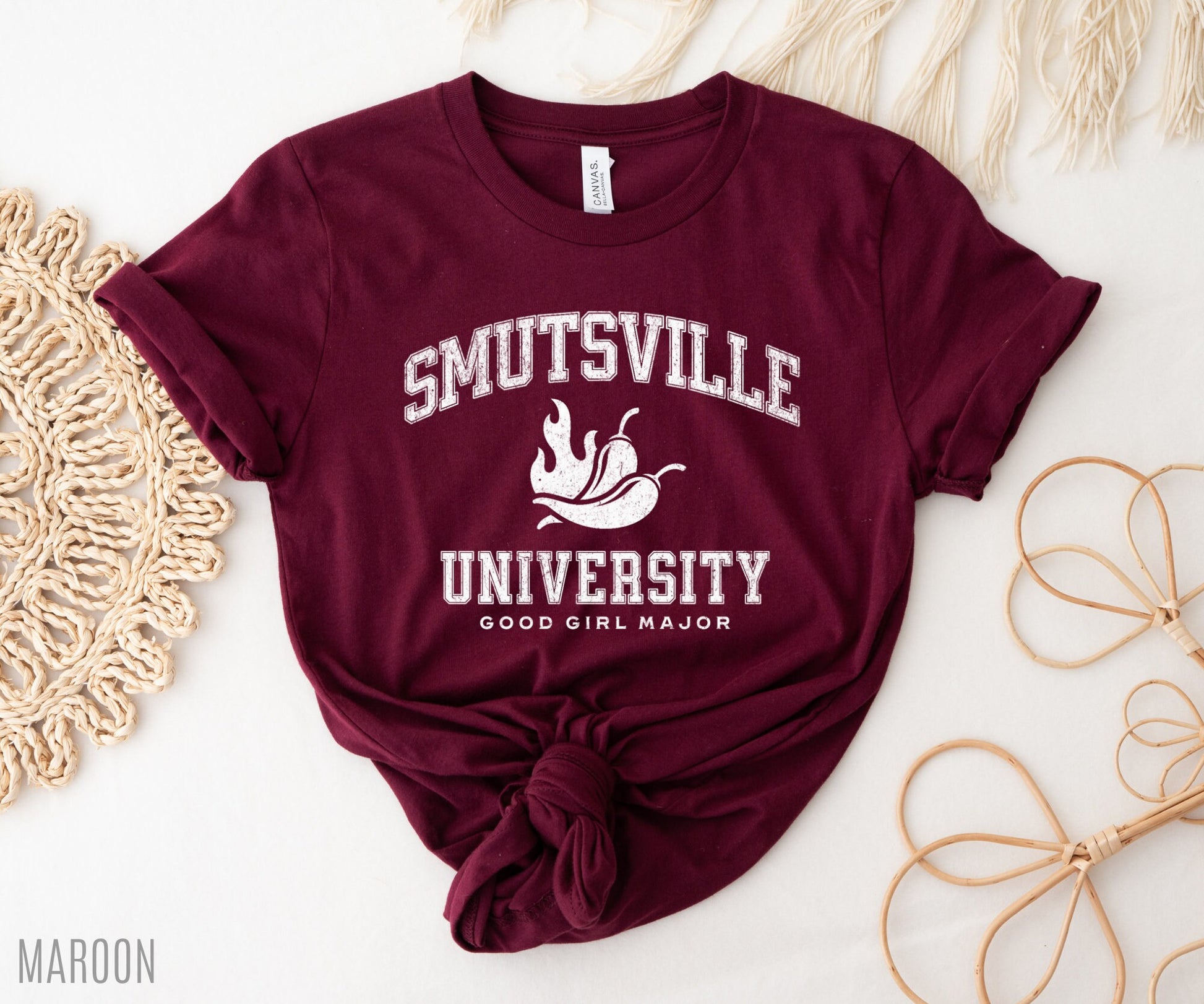 maroon t-shirt with white collegiate “Smutsville University” text, styled with macrame and natural props
