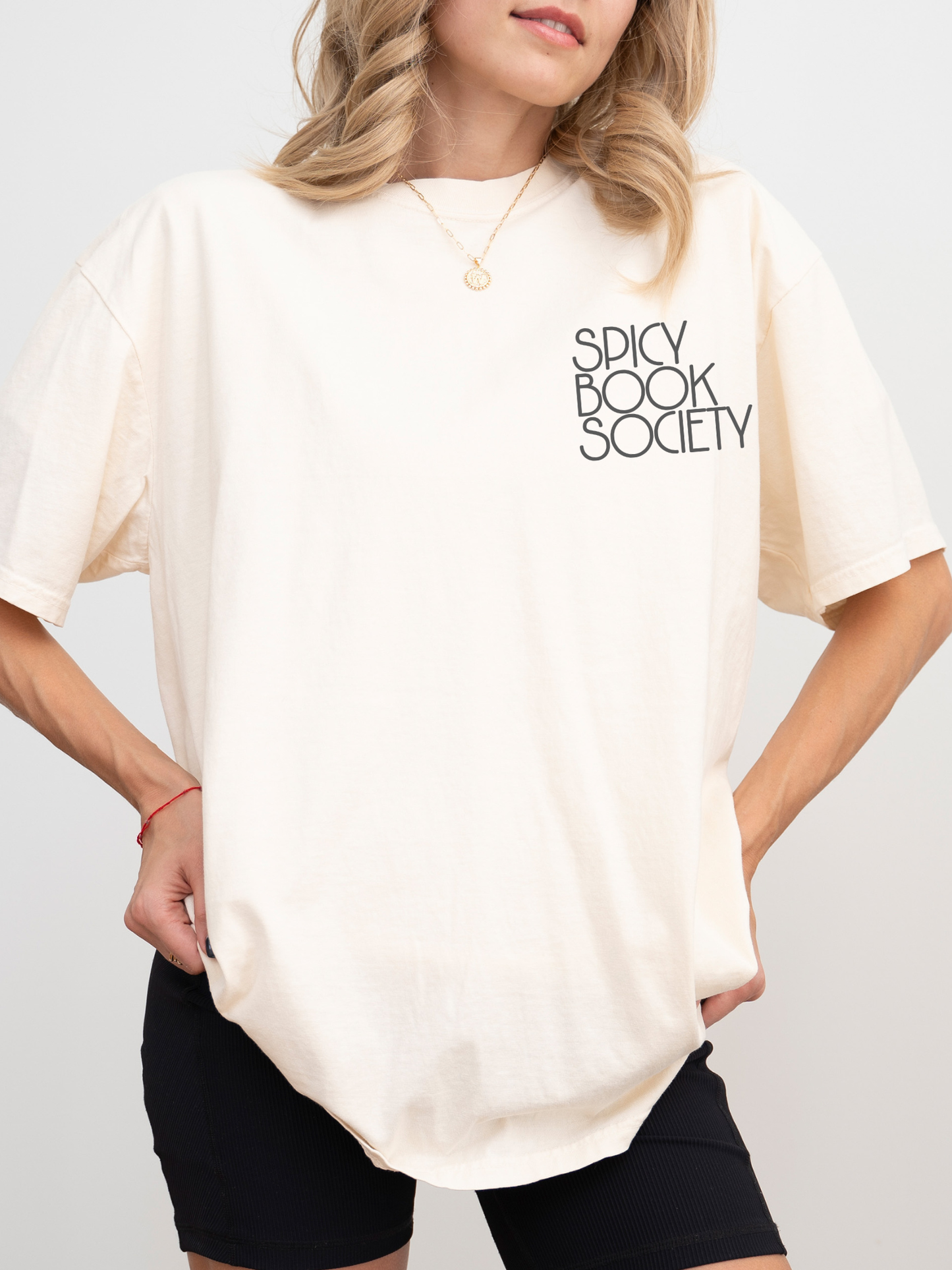 Model wearing a natural ivory Comfort Colors shirt with “Spicy Book Society” printed on the front chest. Styled in a clean, minimal look with biker shorts, soft waves, and gold jewelry — perfect for spicy fiction fans.