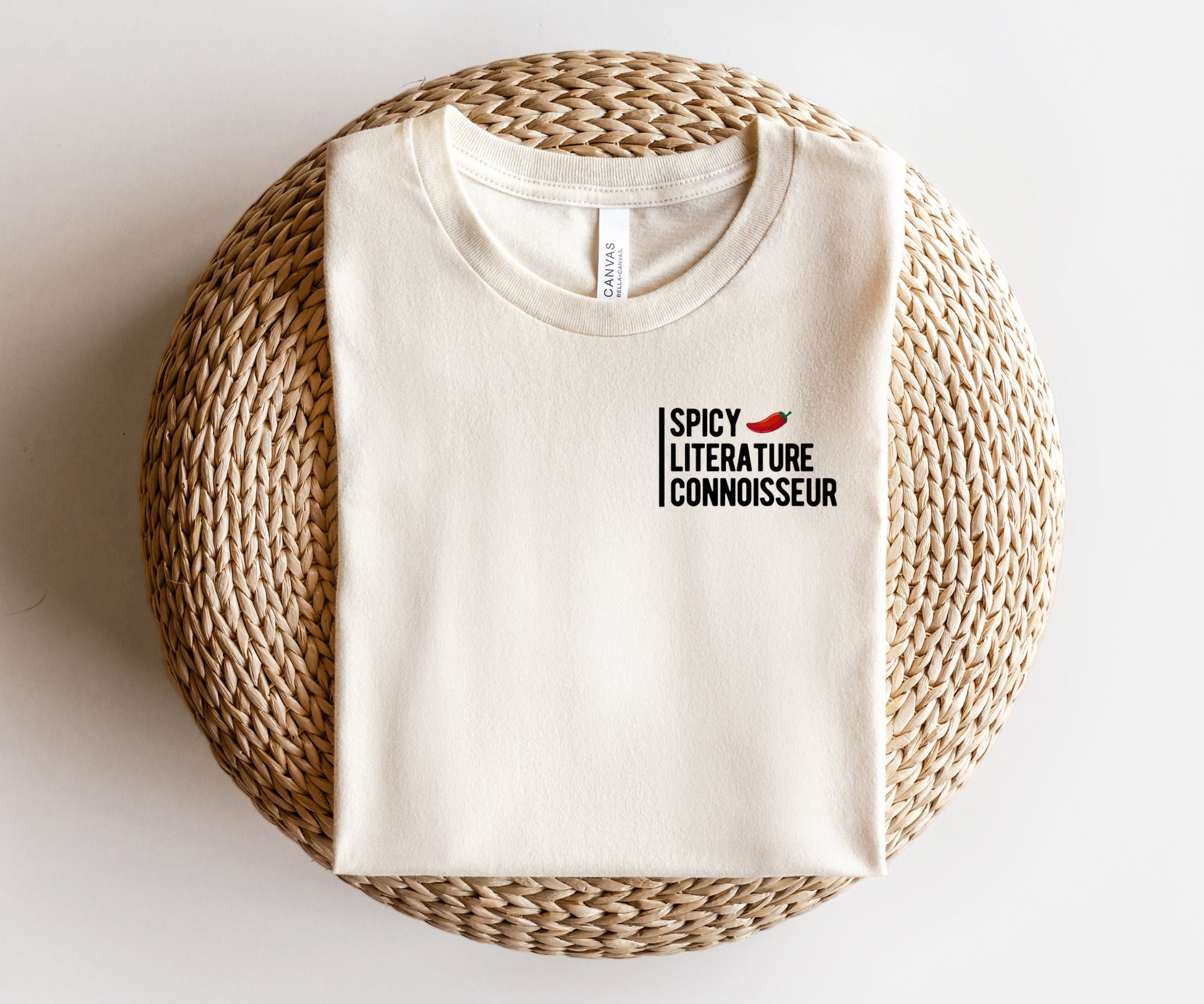 folded cream bookish t-shirt with spicy literature connoisseur text and pepper icon on wicker ottoman