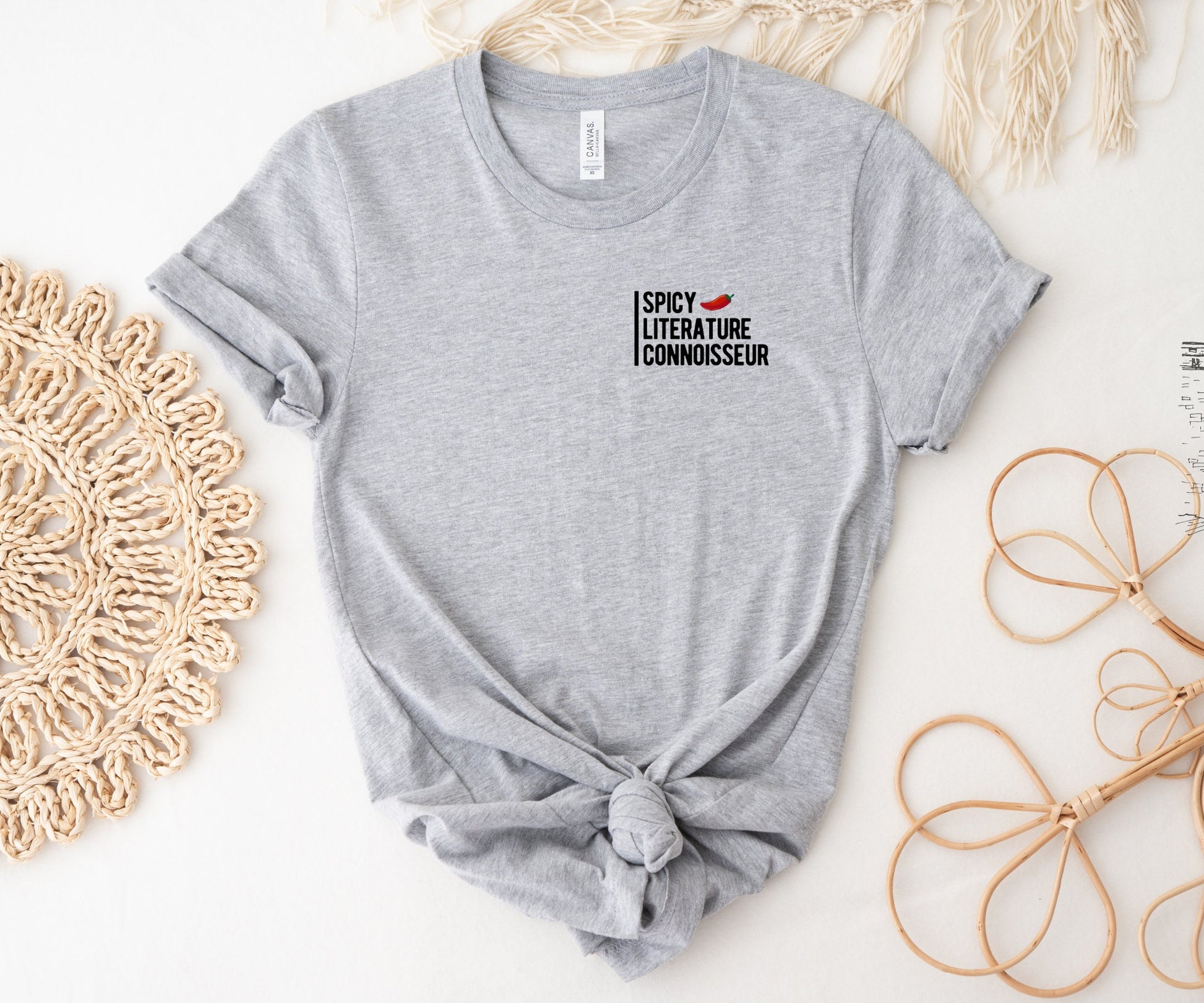 light gray shirt with rolled sleeves and black text spicy literature connoisseur next to decorative boho accents