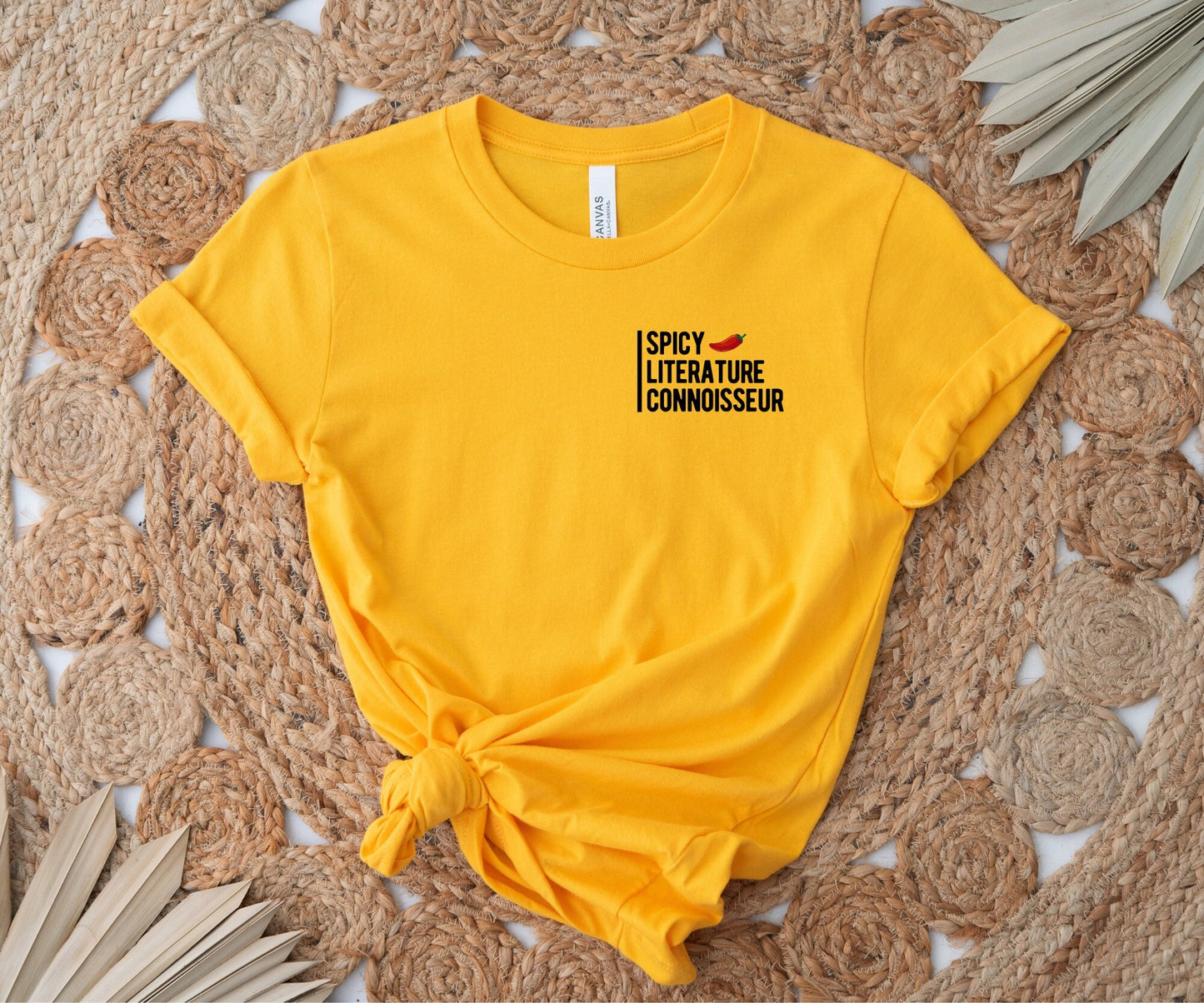 bright yellow t-shirt with black text and red chili pepper that says spicy literature connoisseur on woven rug background