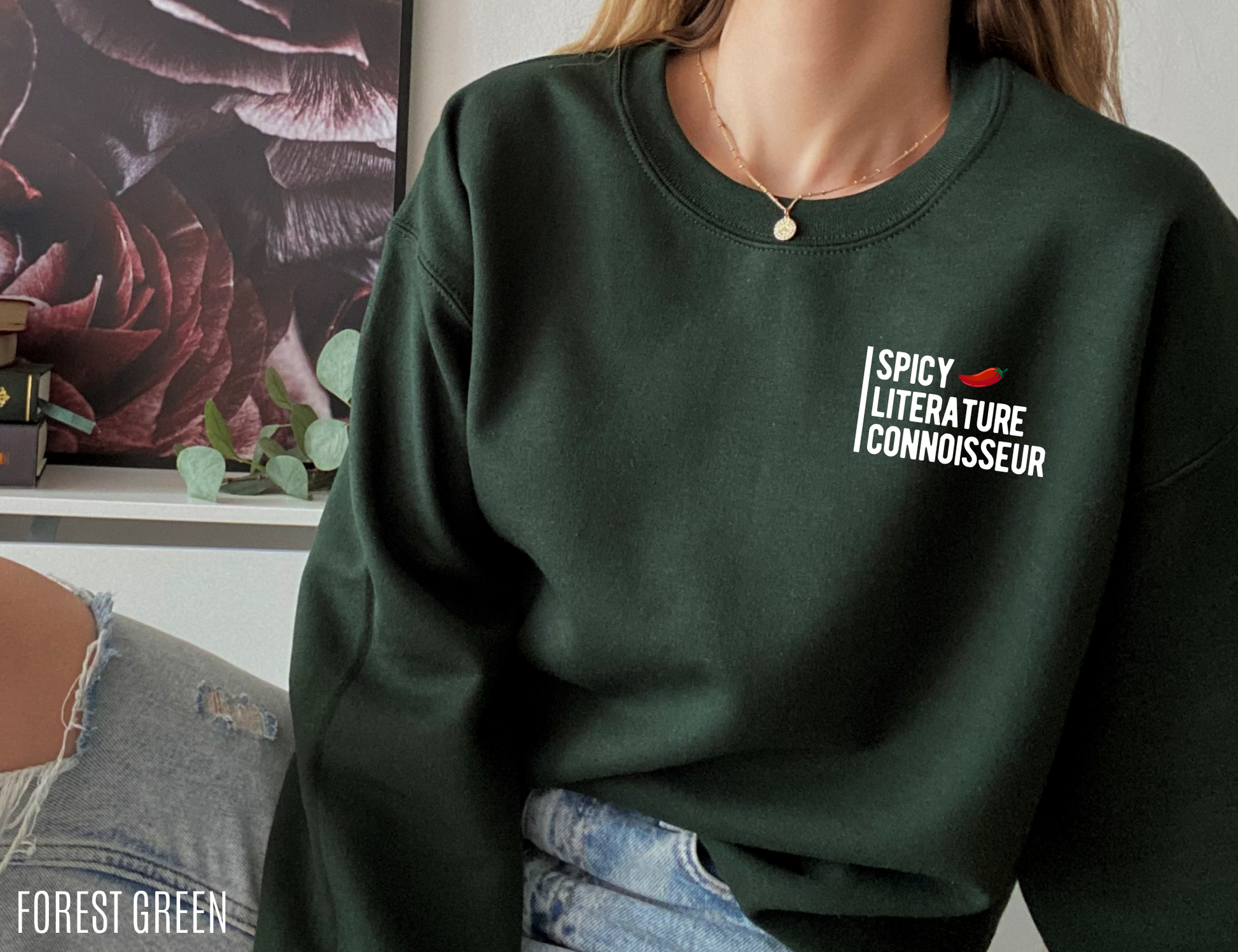 woman wearing forest green sweatshirt with Spicy Literature Connoisseur design sitting near bookshelf