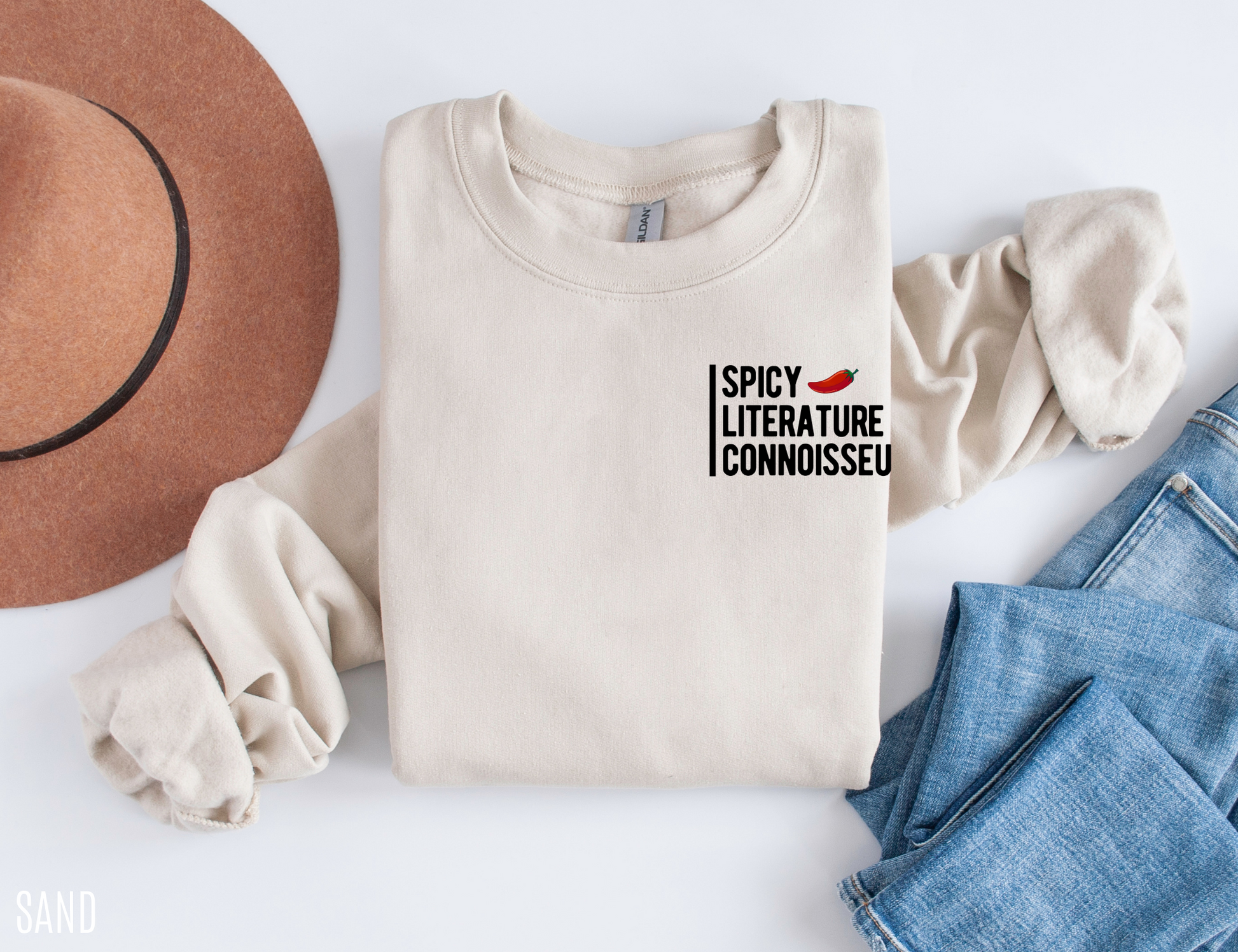 flat lay of sand Spicy Literature Connoisseur sweatshirt styled with hat and light denim