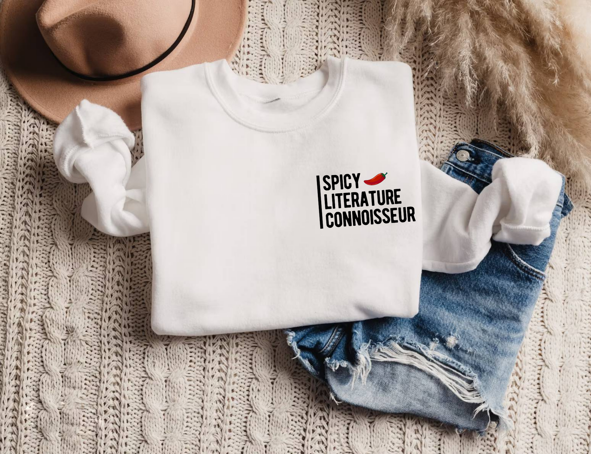 flat lay of white Spicy Literature Connoisseur sweatshirt styled with knit blanket and denim shorts