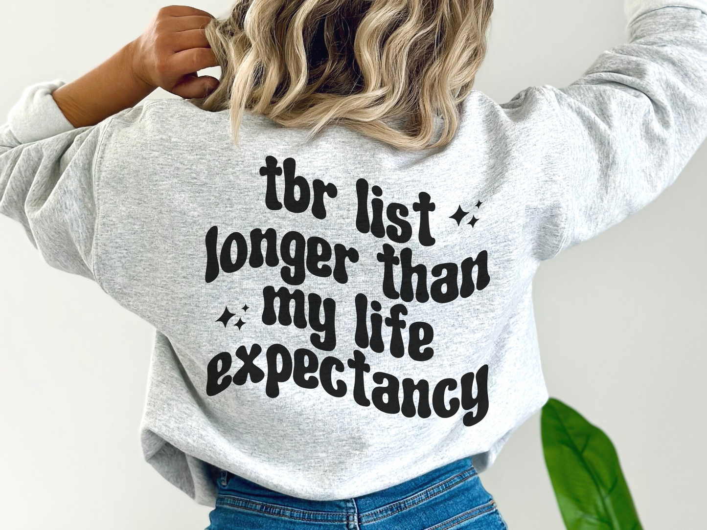 woman in light ash grey sweatshirt with funny TBR quote and cozy bookish vibe