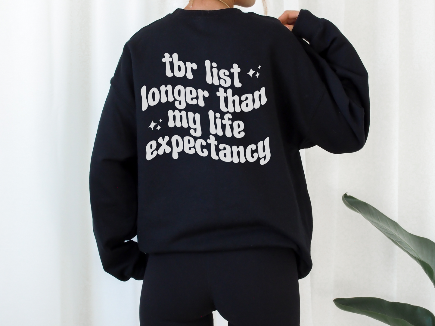 woman wearing oversized black sweatshirt with bold white bookish quote about a long TBR list