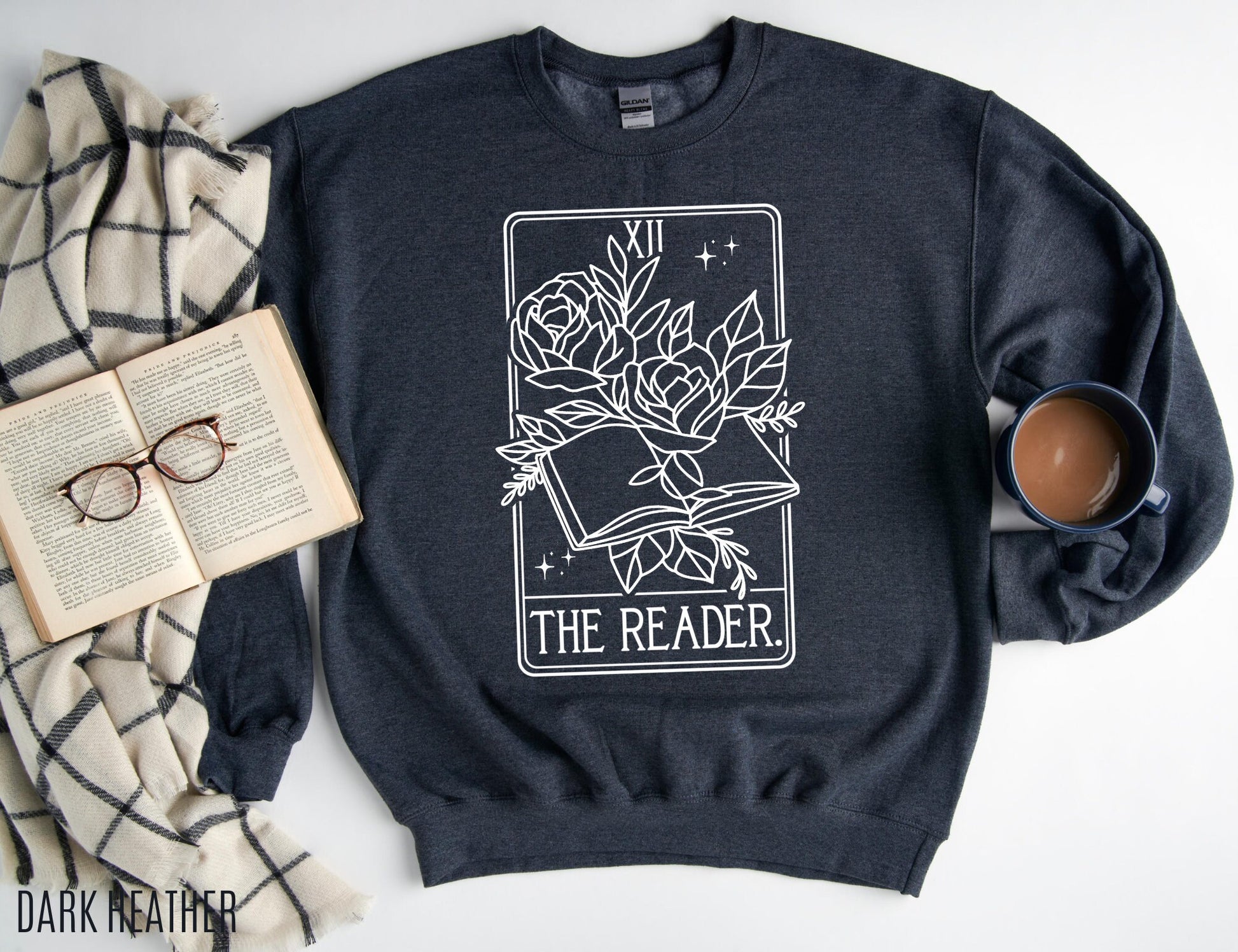flat lay of dark heather The Reader sweatshirt with tarot-style book design, styled with coffee and glasses