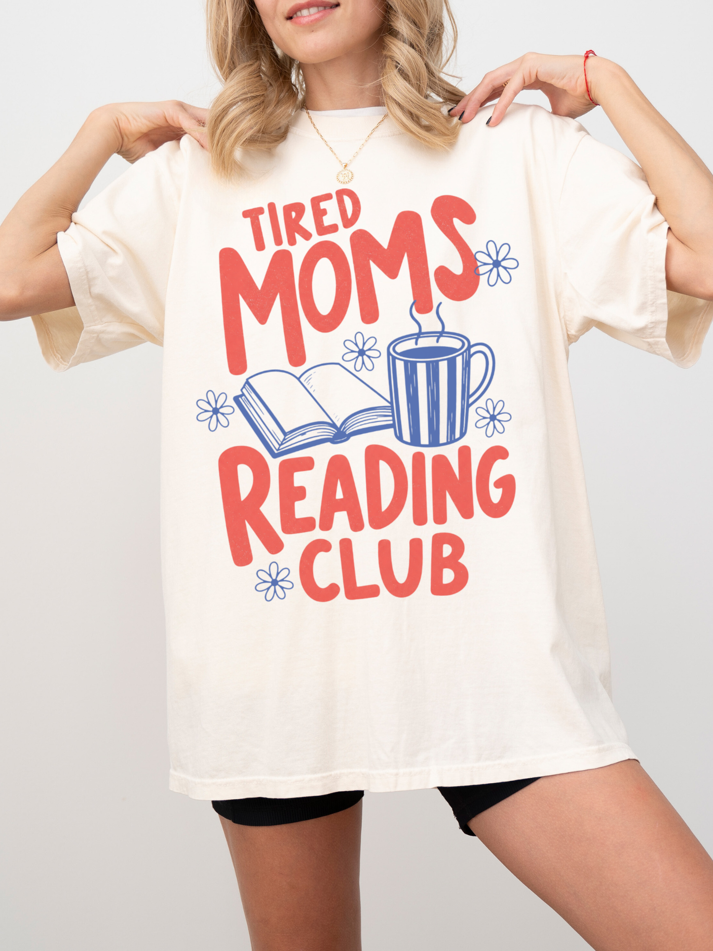 woman wearing oversized natural cream tired moms reading club graphic t shirt with retro typography coffee mug and open book artwork