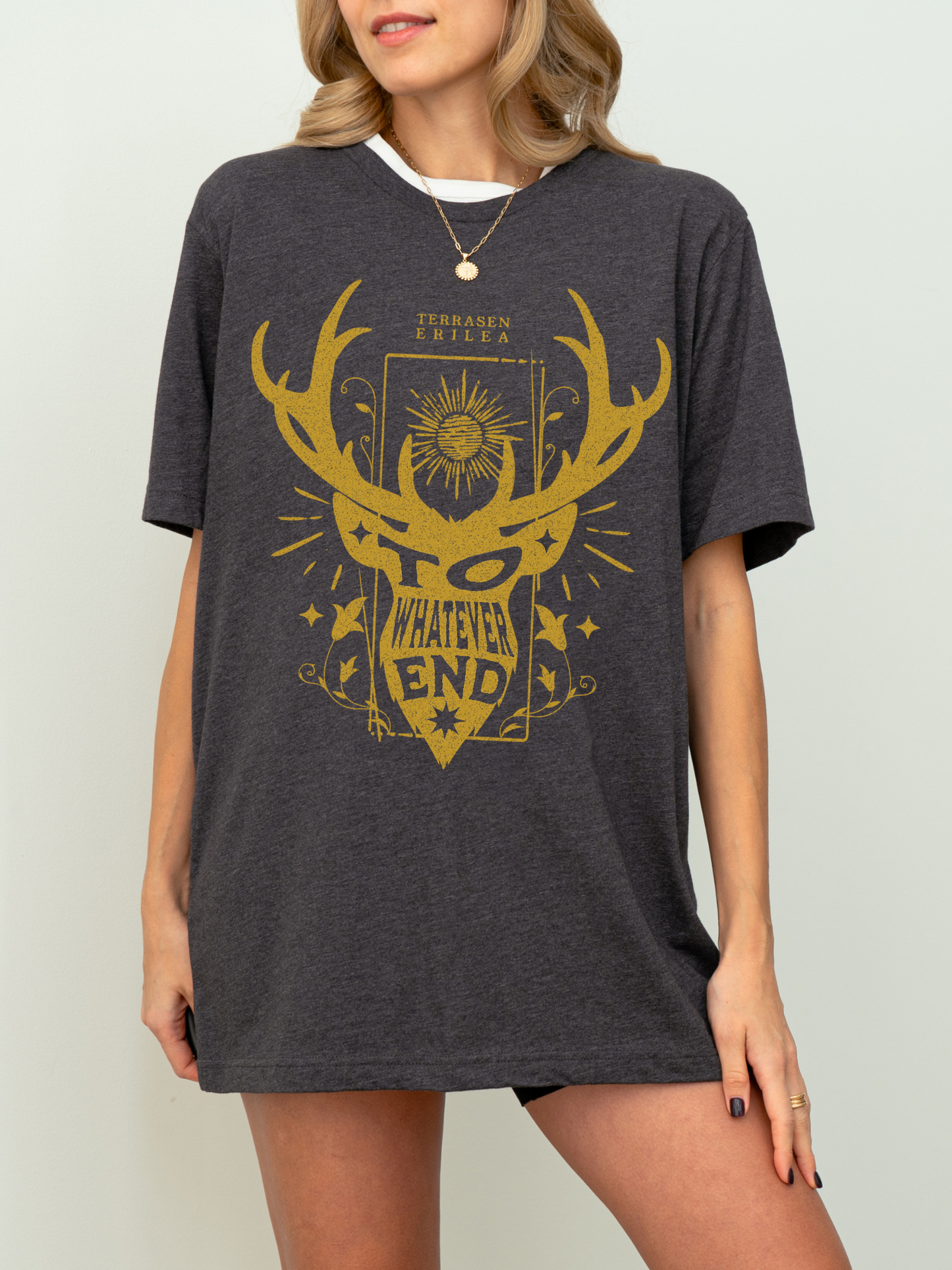 Model in dark heather grey “To Whatever End” t-shirt with fantasy bookish design, styled casually with black shorts indoors