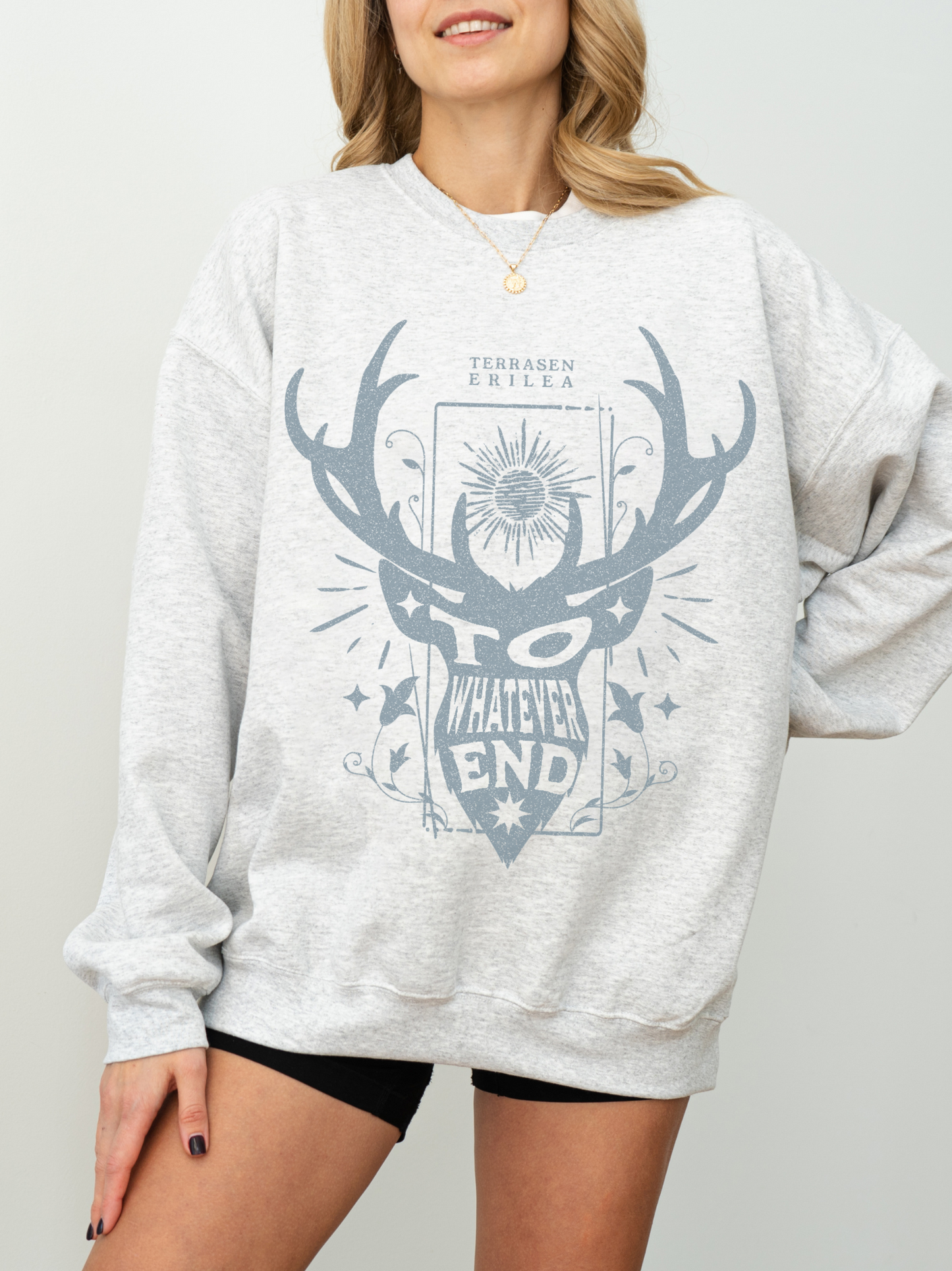 woman in ash grey Throne of Glass sweatshirt with blue Terrasen crest and “To Whatever End” fantasy book quote