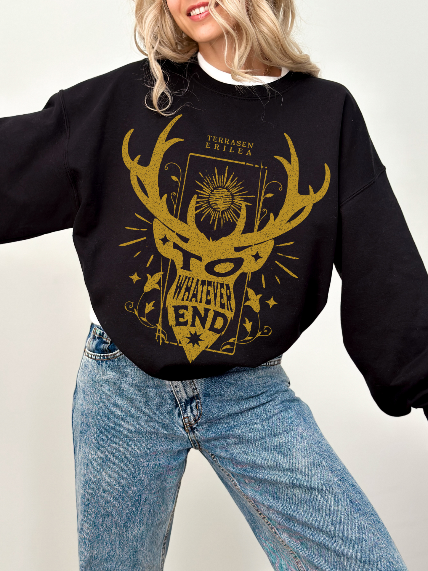 woman in black sweatshirt with gold Terrasen design featuring antlers and “To Whatever End” banner from fantasy book series