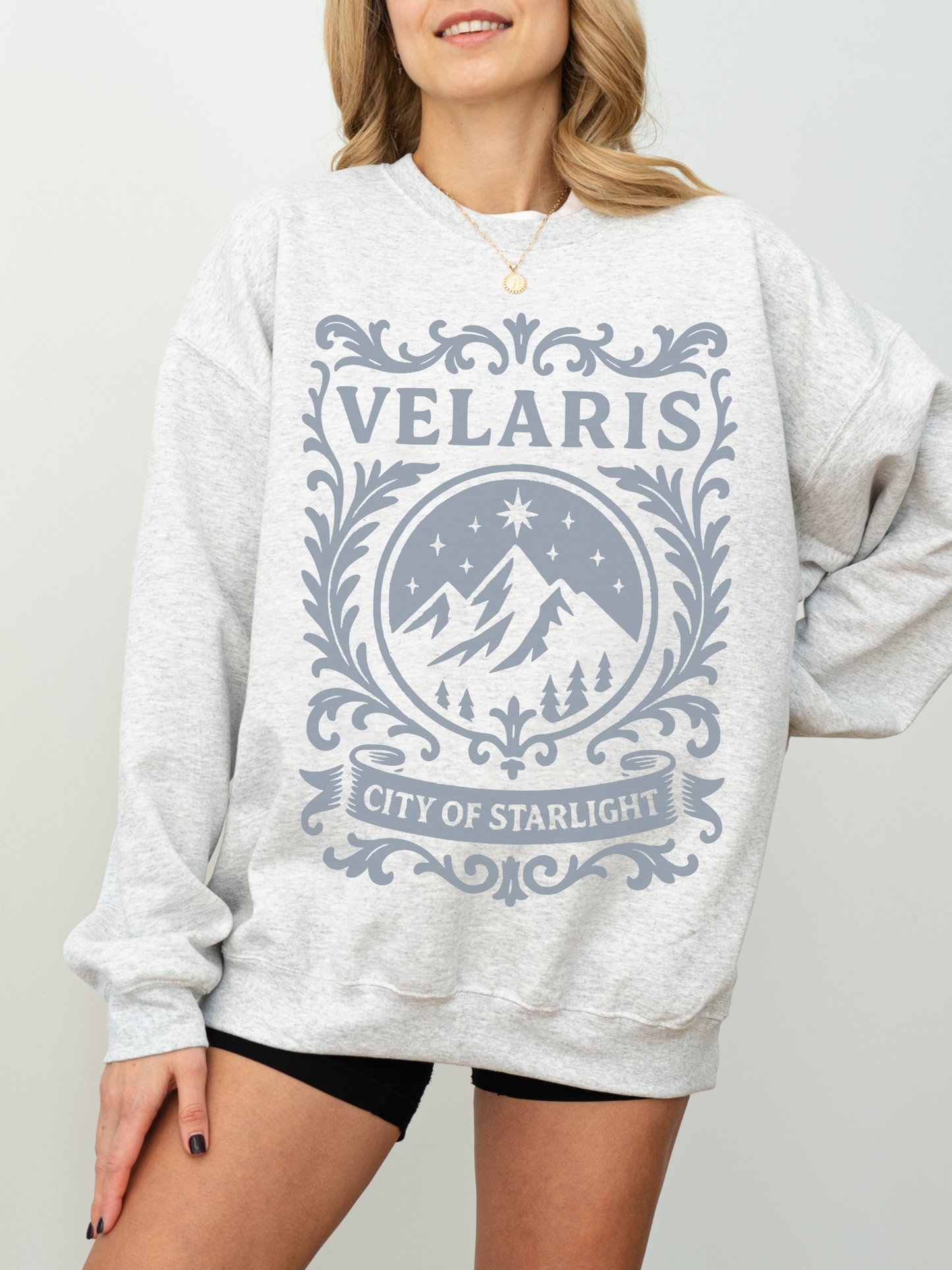 woman in an ash grey Velaris sweatshirt with light blue fantasy design inspired by ACOTAR’s City of Starlight