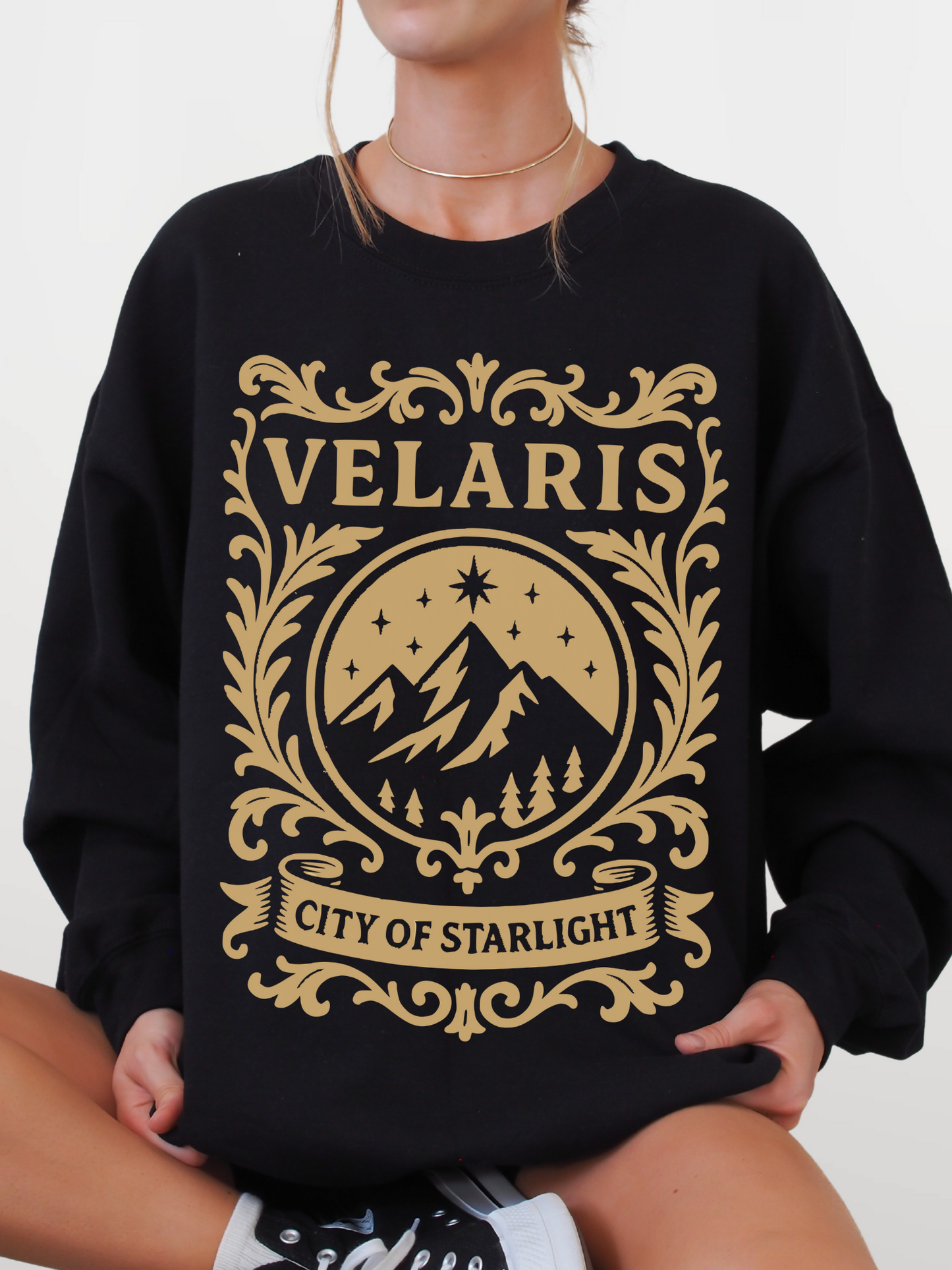 woman in a black sweatshirt with bold gold Velaris City of Starlight fantasy crest design