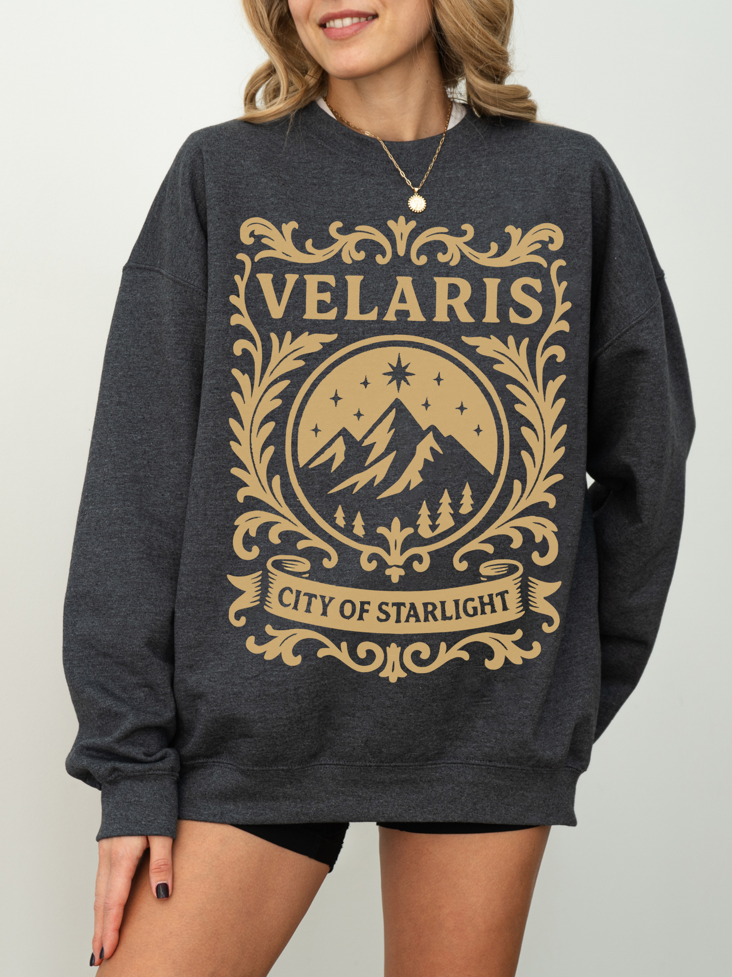 woman wearing a dark heather grey sweatshirt with tan Velaris City of Starlight graphic inspired by the Night Court